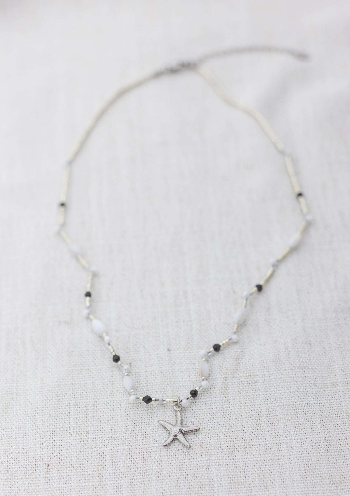 Intuitive Charms Ceto's Song Black tourmaline Braided natural Crystal beaded custom necklace in silver and black cord on a light fabric background rectangle version