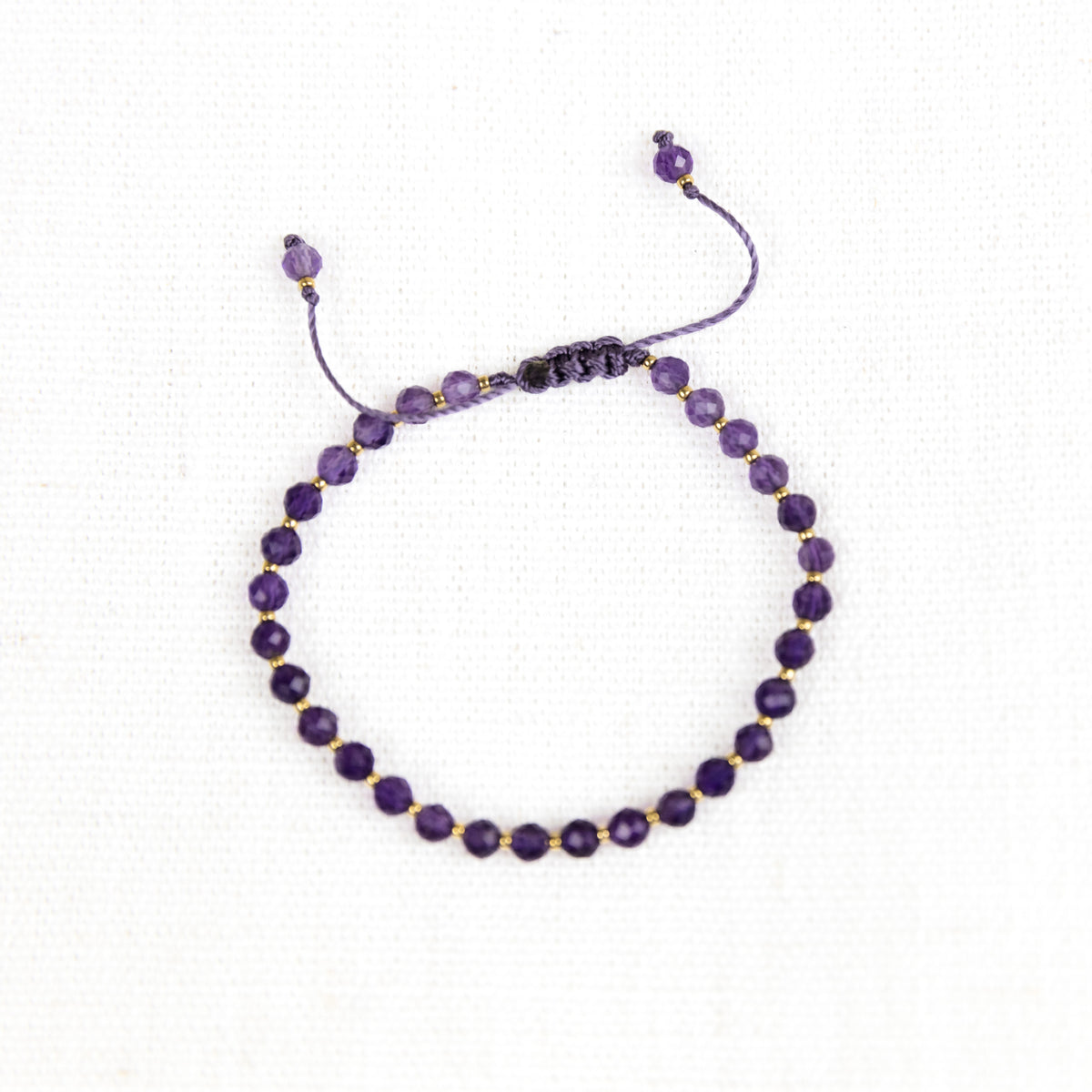 Intuitive Charms Sophia's Glow Amethyst Braided natural Crystal beaded custom Bracelet in gold and purple cord and adjustable clasp extension on a light fabric background