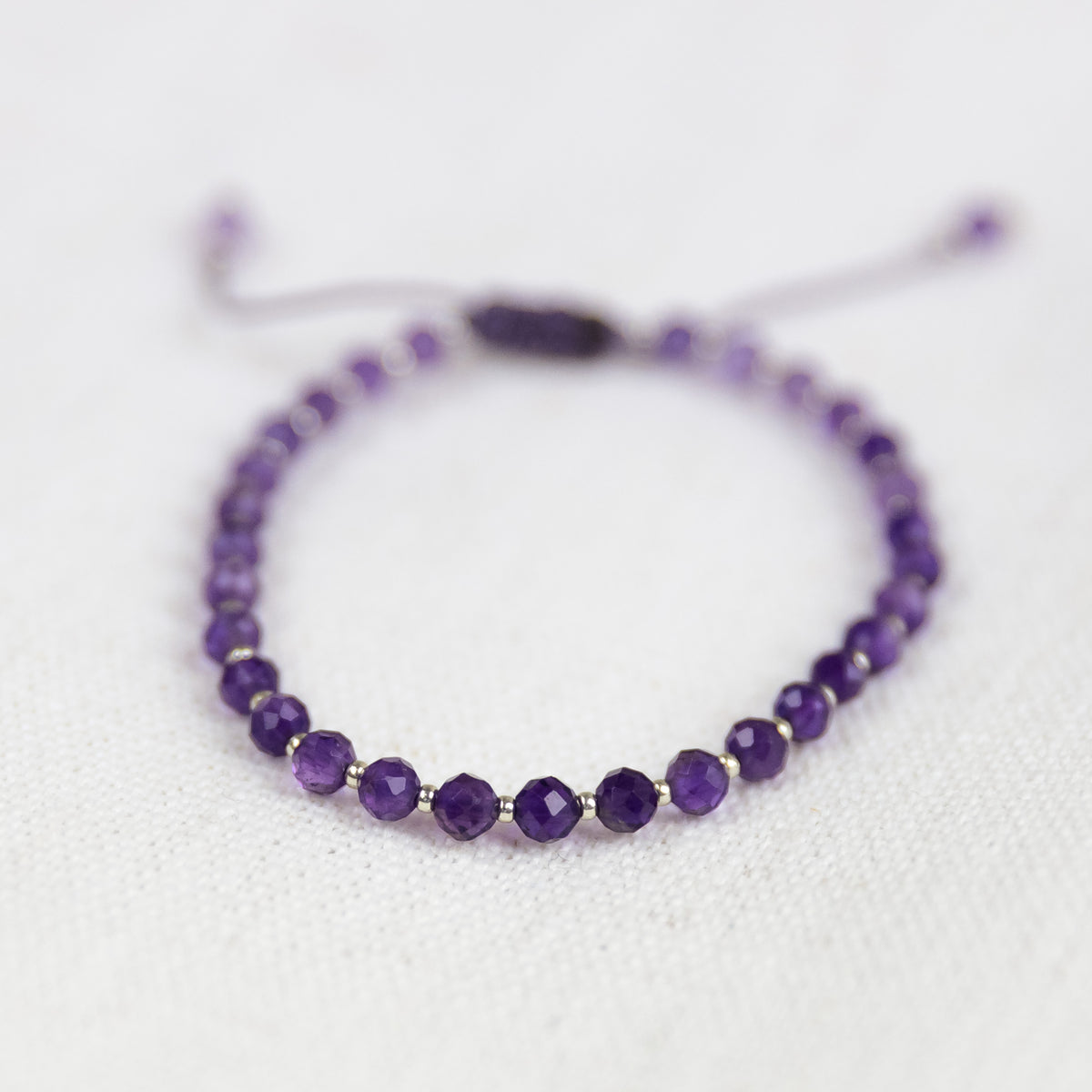 Intuitive Charms Sophia's Glow Amethyst Braided natural Crystal faceted beaded custom Bracelet in silver and purple cord and adjustable clasp extension on a light fabric background zoomed up