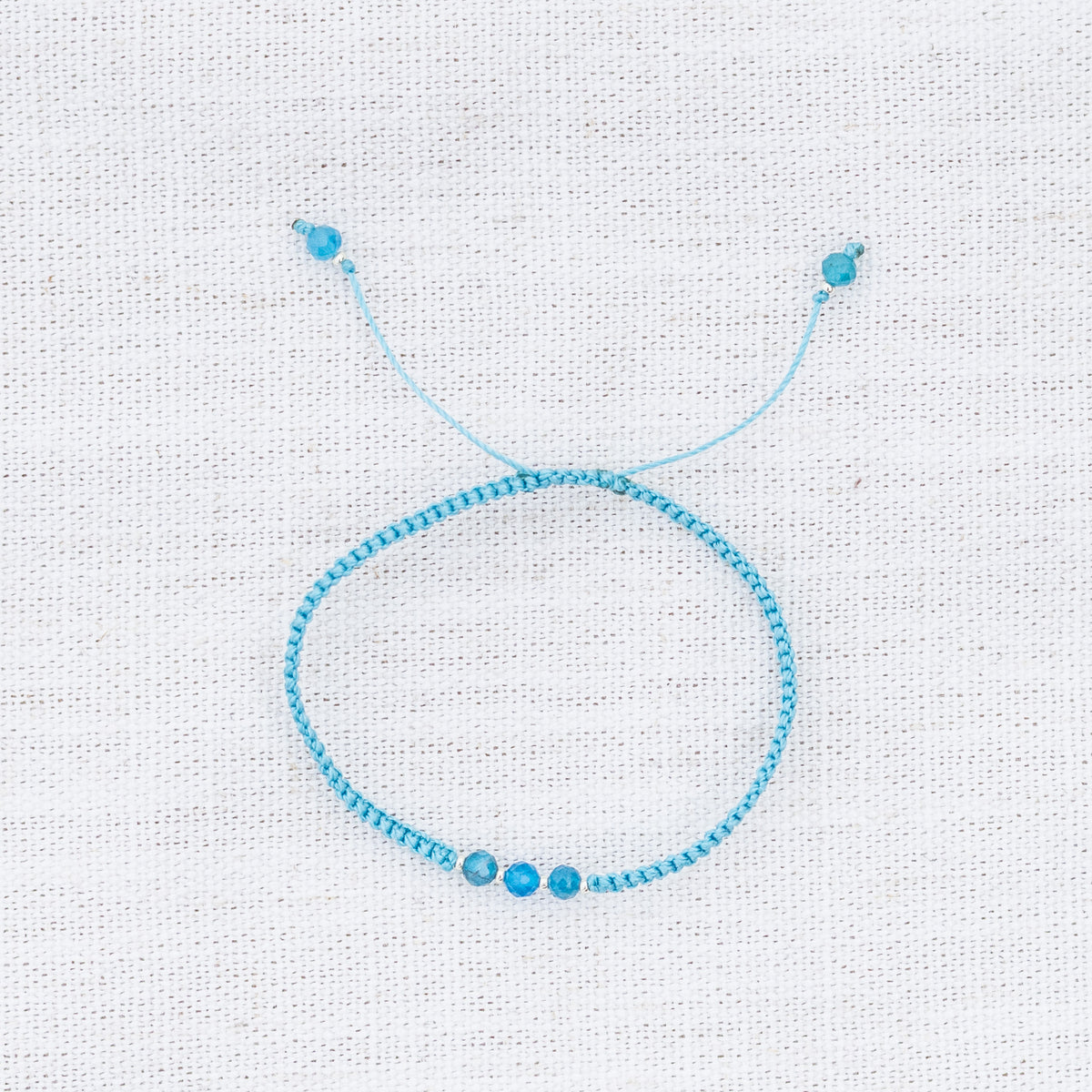 Intuitive Charms Delphina's Guard Apatite Braided natural Crystal beaded custom Bracelet in silver and blue cord on a light fabric background