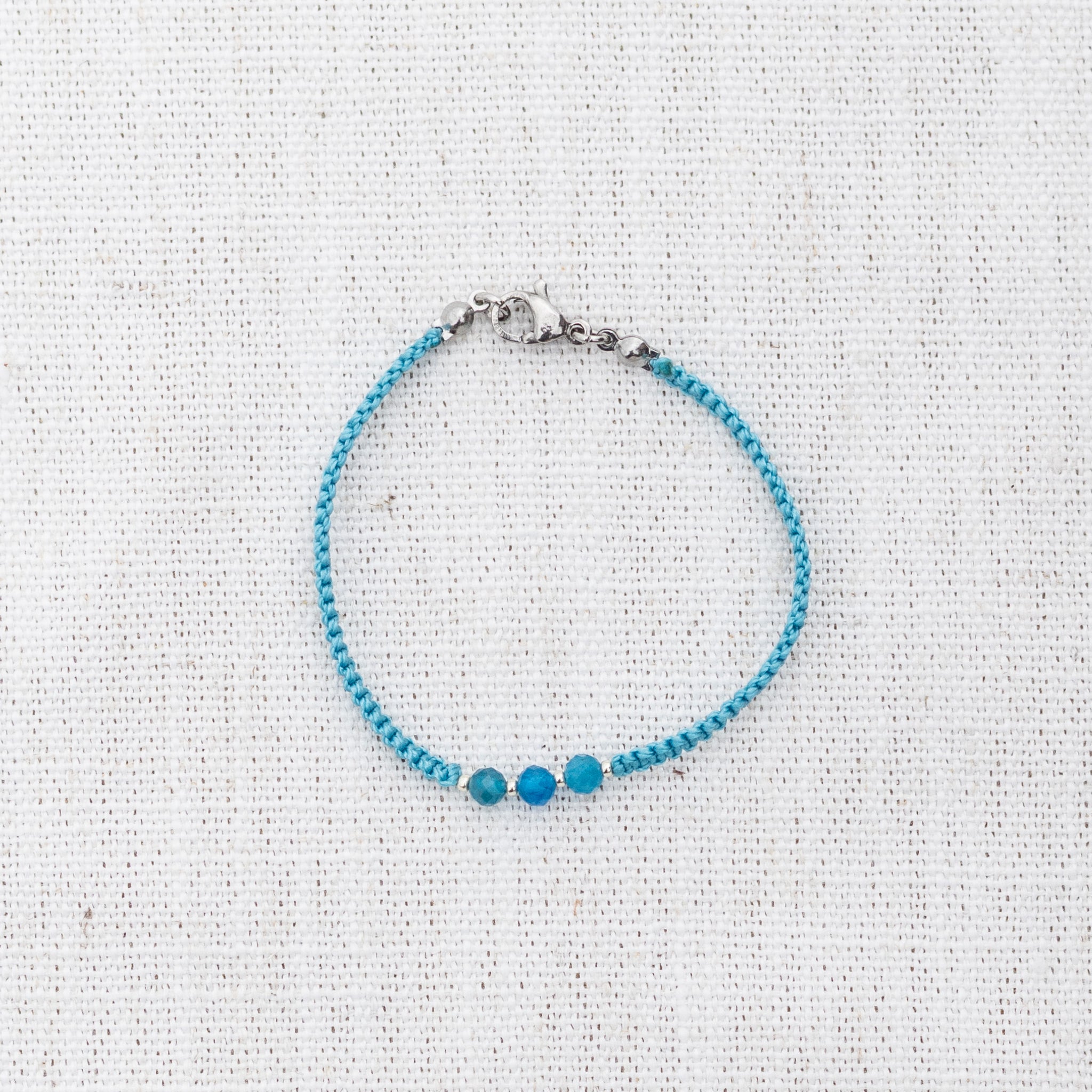 Intuitive Charms Delphina's Guard Apatite Braided natural Crystal beaded custom Bracelet in silver and blue cord and clasp on a light fabric background