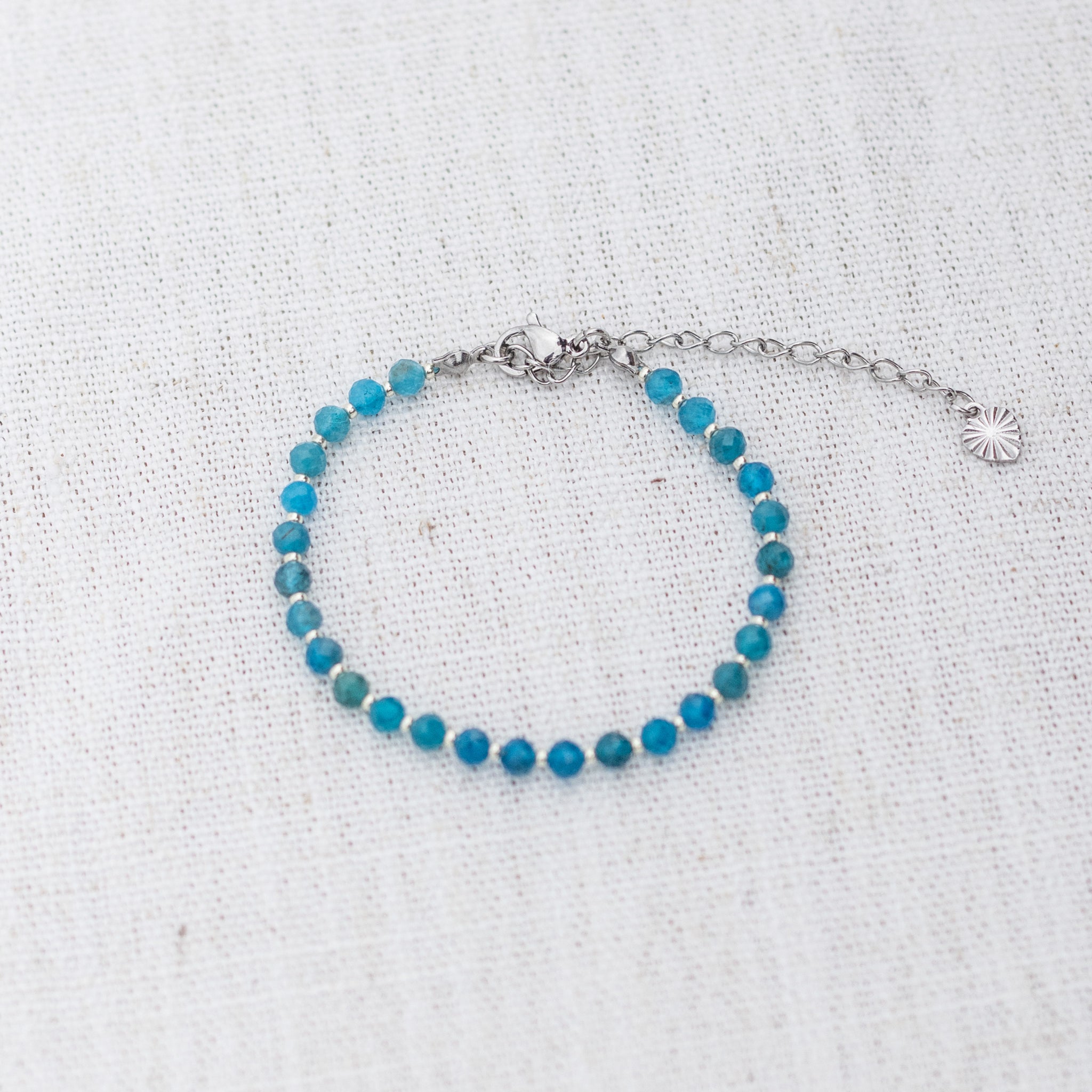 Intuitive Charms Delphina's Glow Apatite Braided natural Crystal beaded custom Bracelet in silver and blue cord and clasp extension on a light fabric background