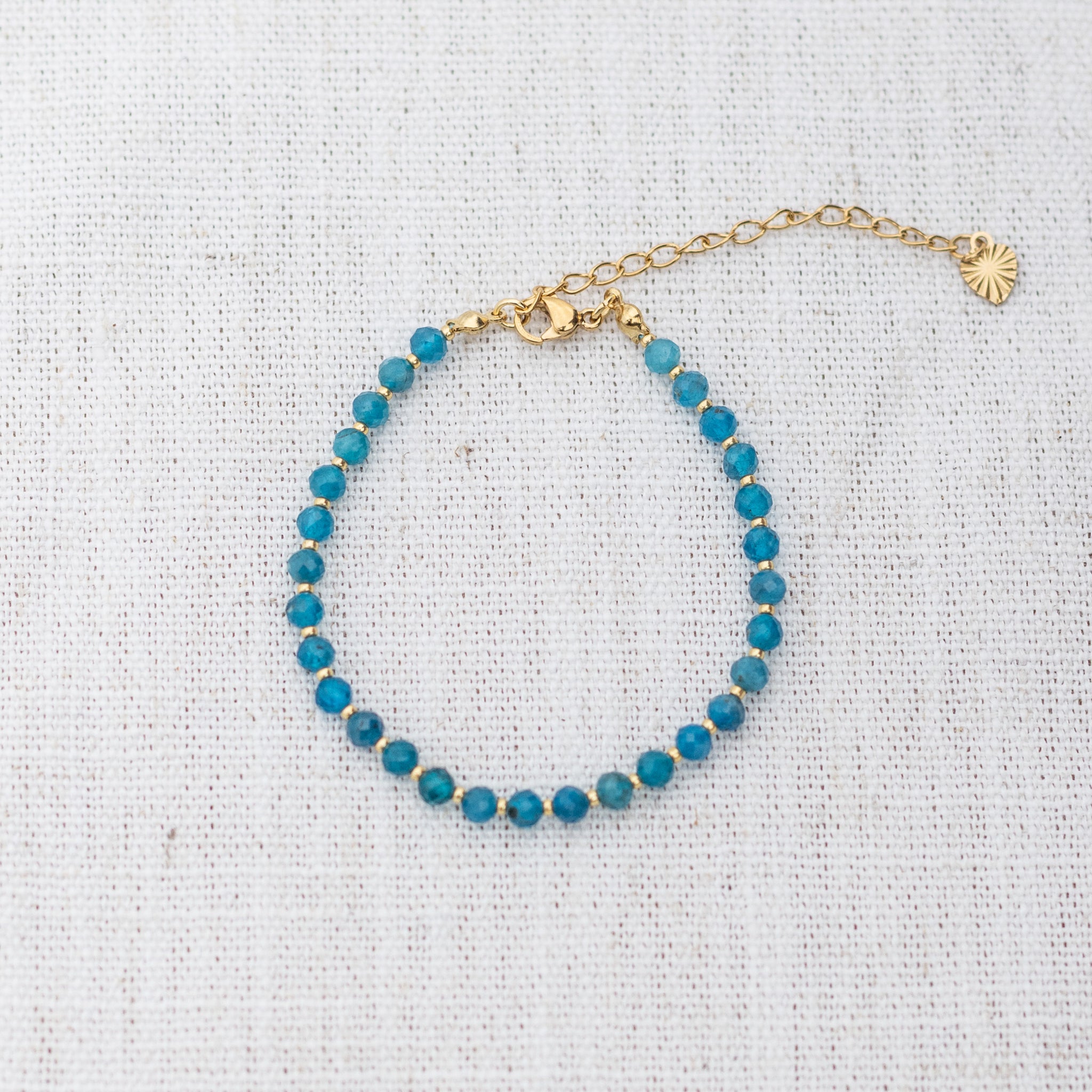 Intuitive Charms Delphina's Glow Apatite Braided natural Crystal beaded custom Bracelet in gold and blue cord and clasp extension on a light fabric background