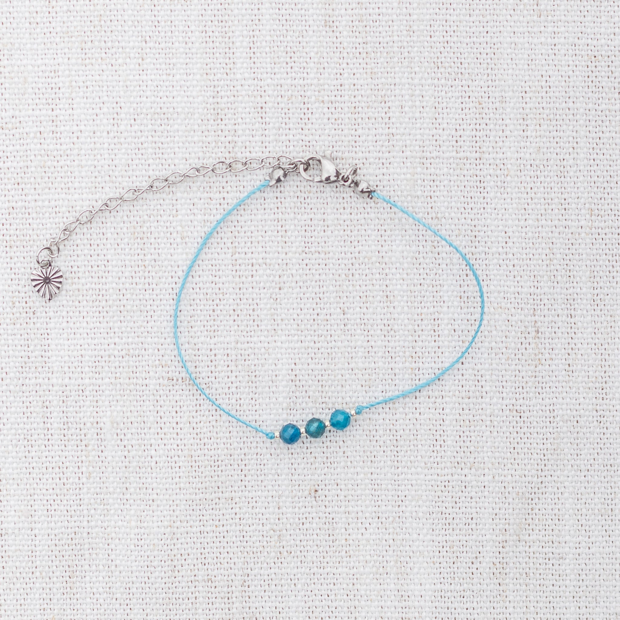 Intuitive Charms Delphina's Mist Apatite Braided natural Crystal beaded custom Bracelet in silver and blue cord and clasp extension on a light fabric background