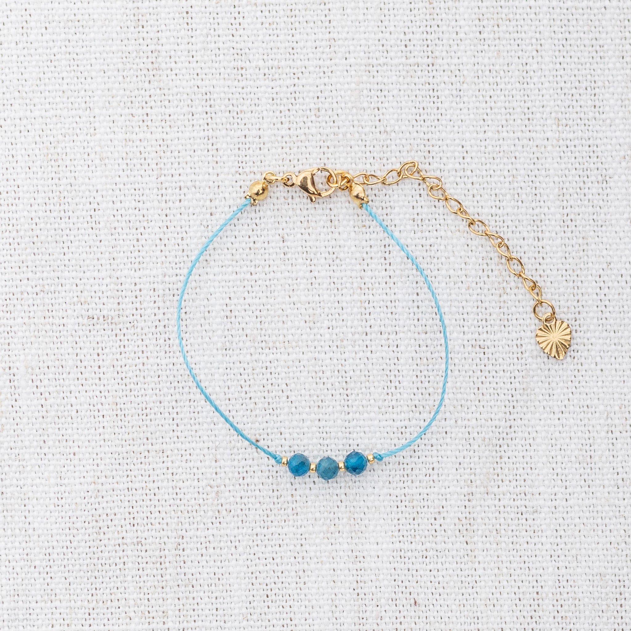 Intuitive Charms Delphina's Mist Apatite Braided natural Crystal beaded custom Bracelet in gold and blue cord and clasp extension on a light fabric background