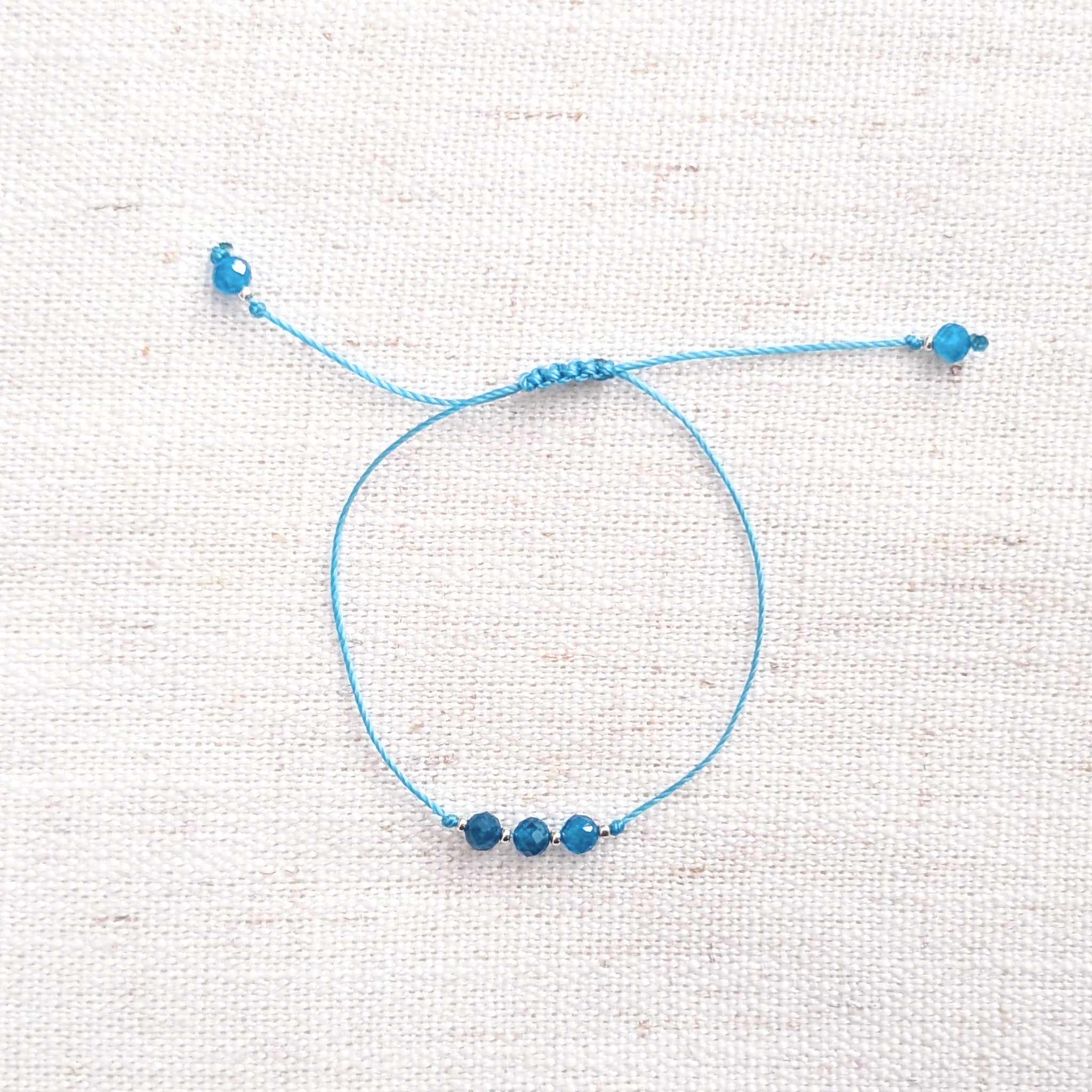 Intuitive Charms Delphina's Mist Apatite Braided natural Crystal beaded custom Bracelet in silver and blue cord on a light fabric background
