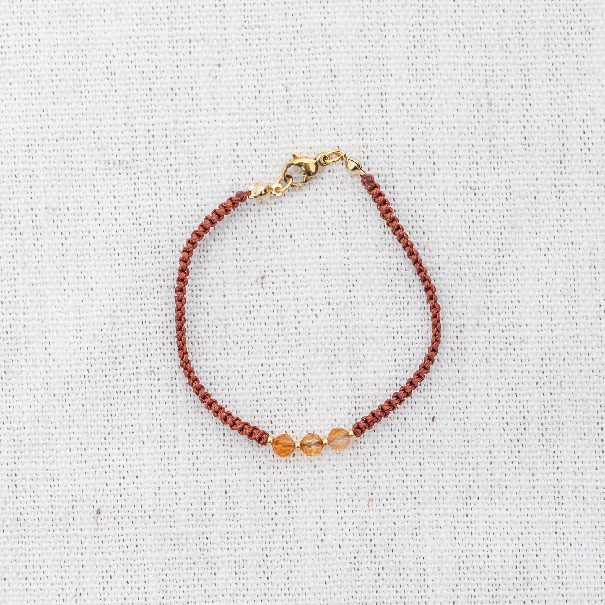 Intuitive Charms Coralia's Guard Carnelian Braided natural Crystal beaded custom Bracelet in silver and red cord and gold clasp on light fabric background