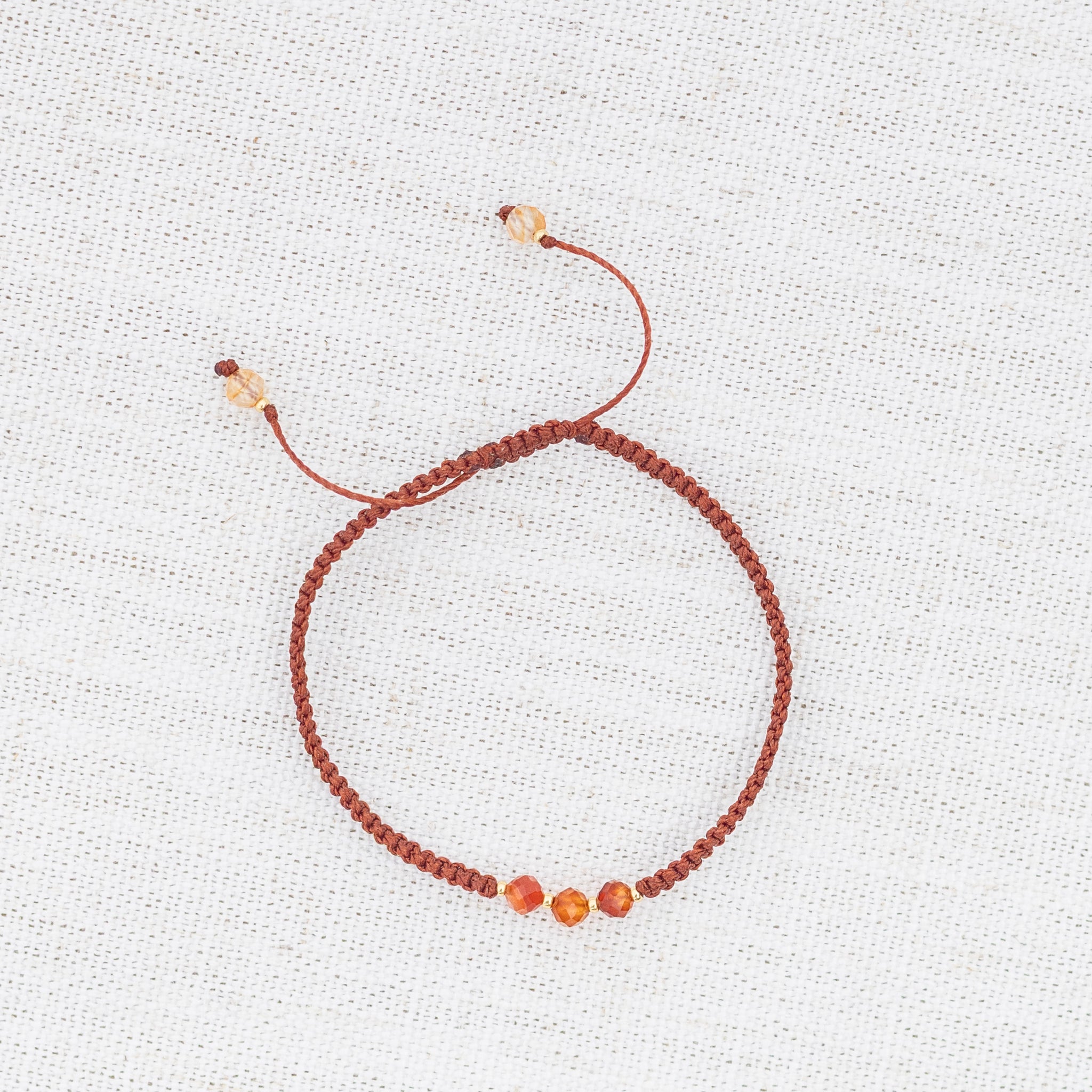 Intuitive Charms Coralia's Guard Carnelian Braided natural Crystal beaded custom Bracelet in gold and red cord on light fabric background
