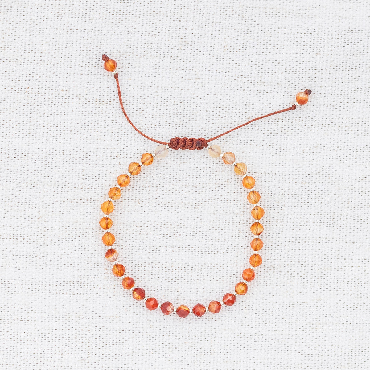 Intuitive Charms Coralia's Glow Carnelian Braided natural Crystal beaded custom Bracelet in silver and red cord on light fabric background