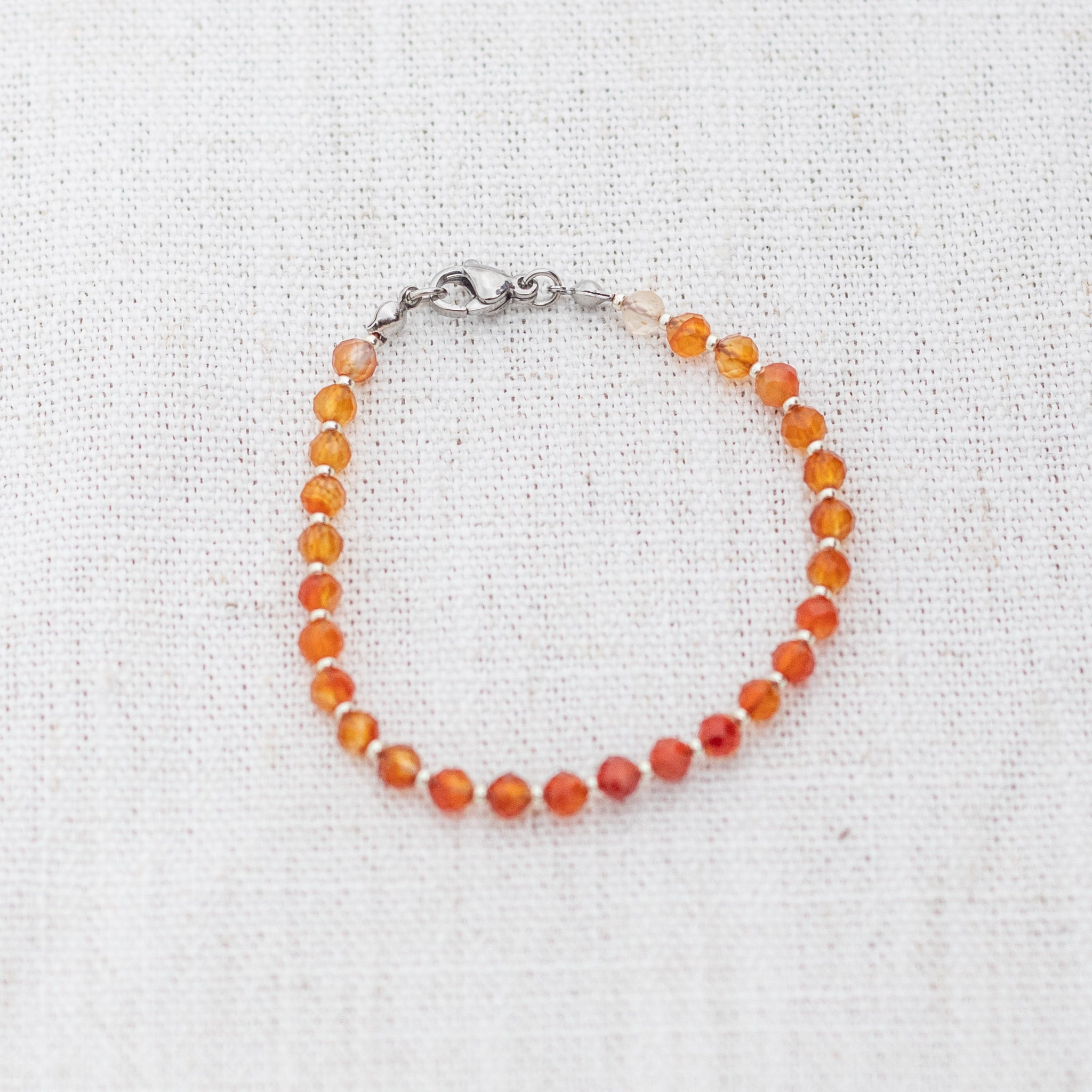 Intuitive Charms Coralia's Glow Carnelian Braided natural Crystal beaded custom Bracelet in silver and red cord and clasp on a light fabric background