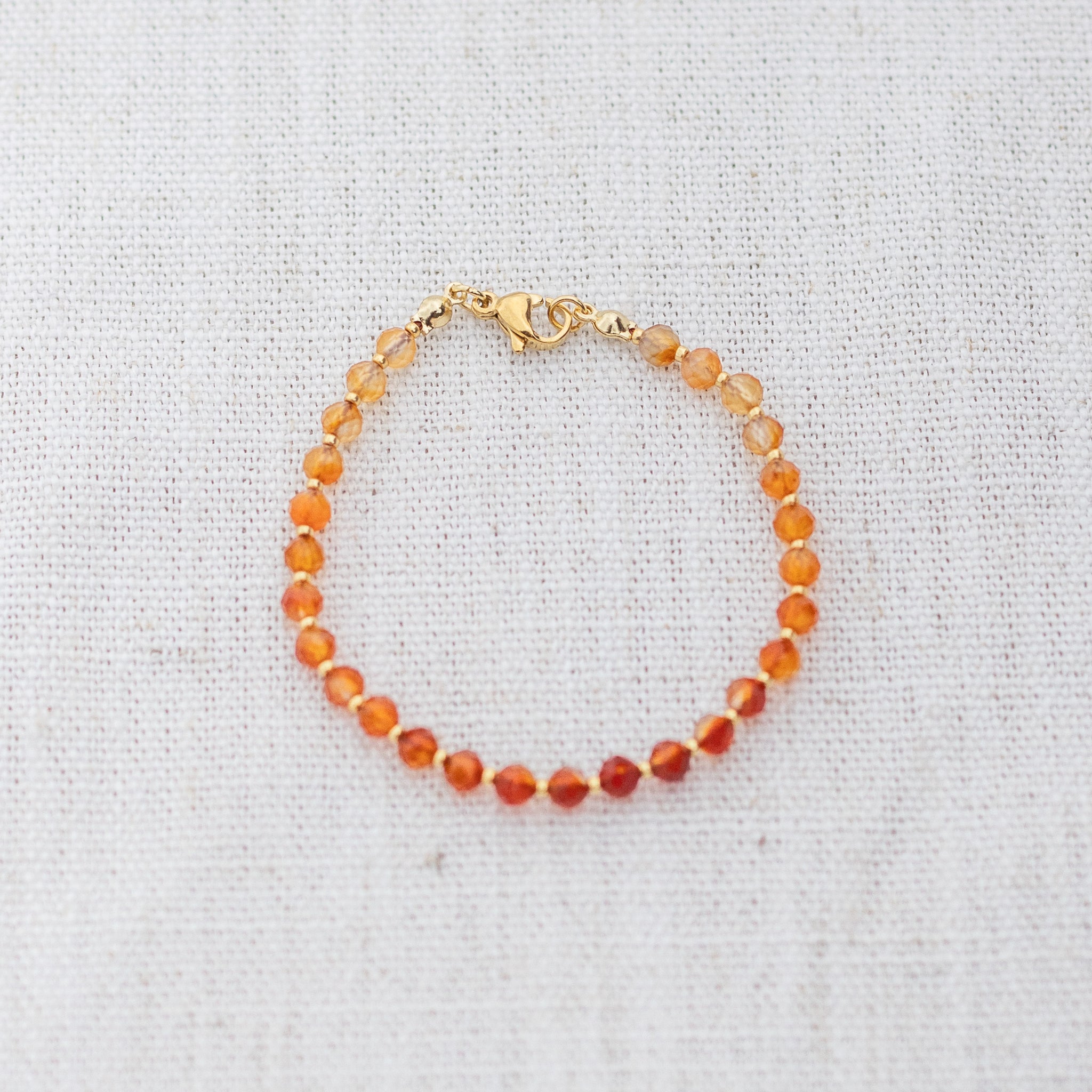 Intuitive Charms Coralia's Glow Carnelian Braided natural Crystal beaded custom Bracelet in gold and red cord and clasp on a light fabric background
