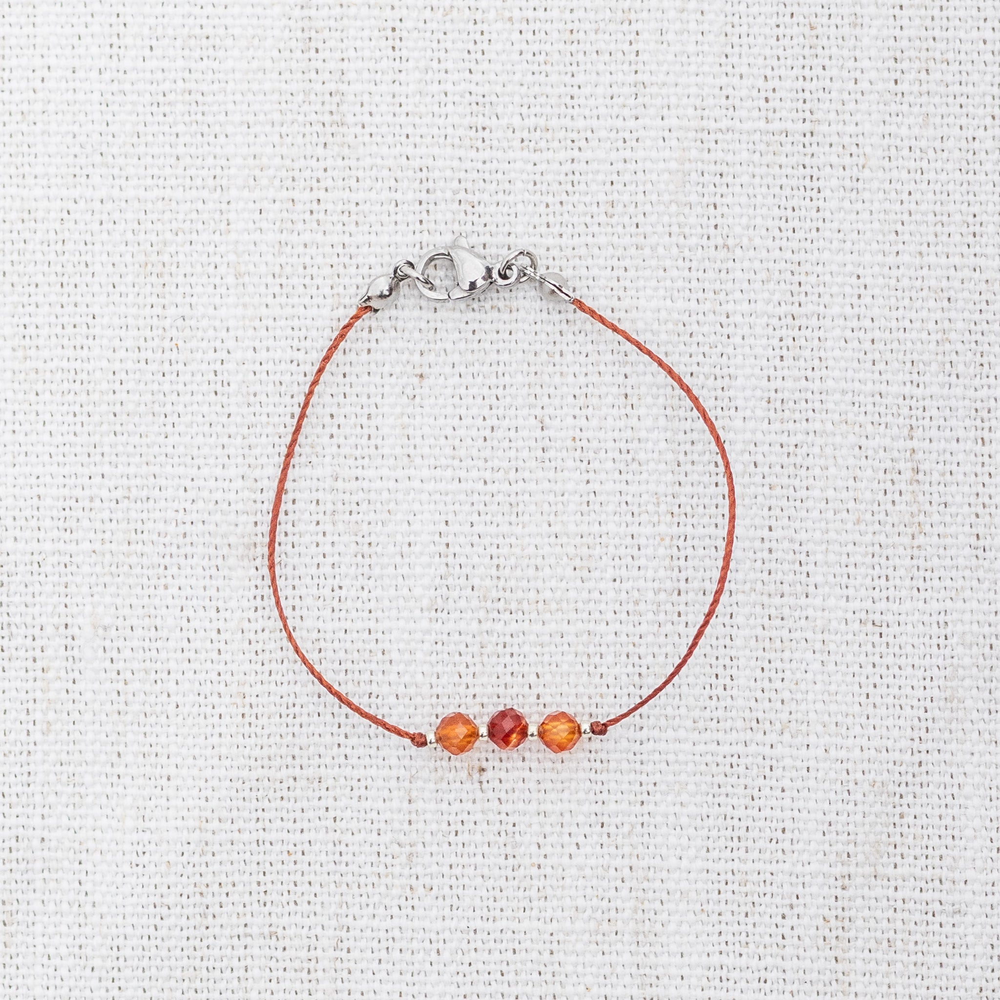 Intuitive Charms Coralia's Mist Carnelian Braided natural Crystal beaded custom Bracelet in silver and red cord and clasp on light fabric background