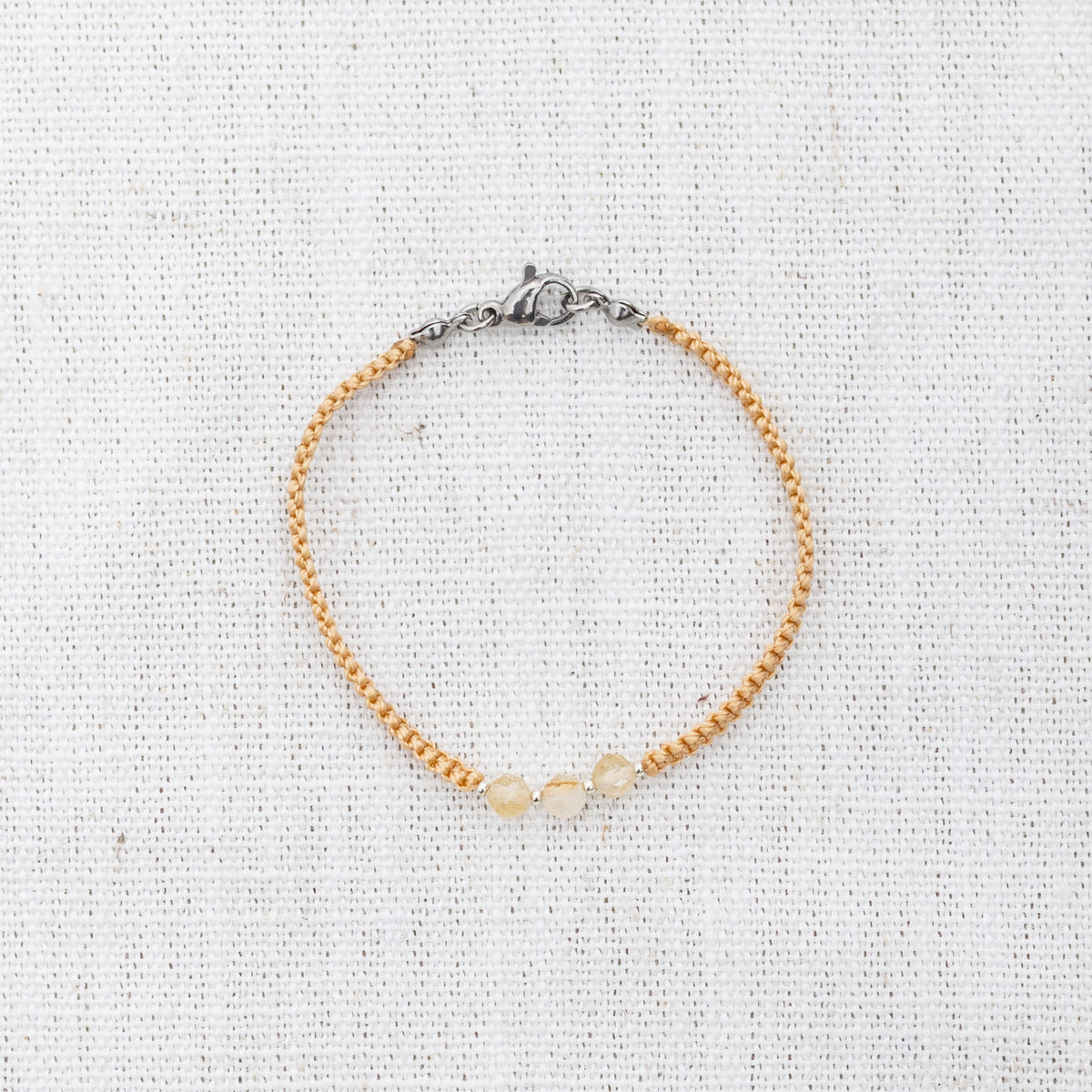 Intuitive Charms Eos's Guard Citrine Braided natural Crystal beaded custom Bracelet in silver and yellow cord and clasp on a light fabric background