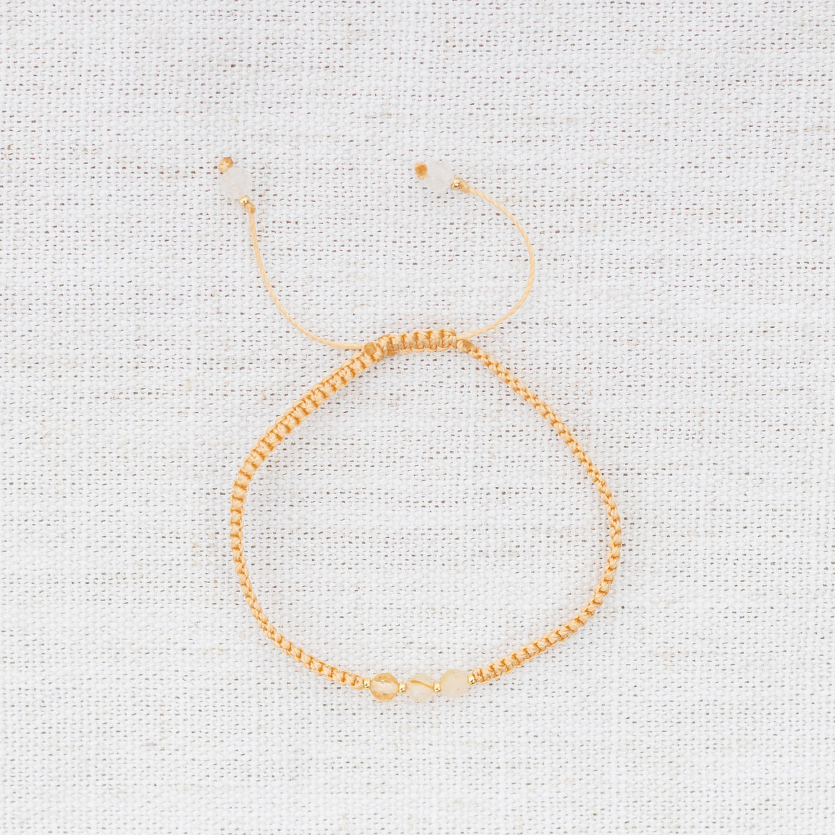 Intuitive Charms Eos's Guard Citrine Braided natural Crystal beaded custom Bracelet in gold and yellow cord on a light fabric background