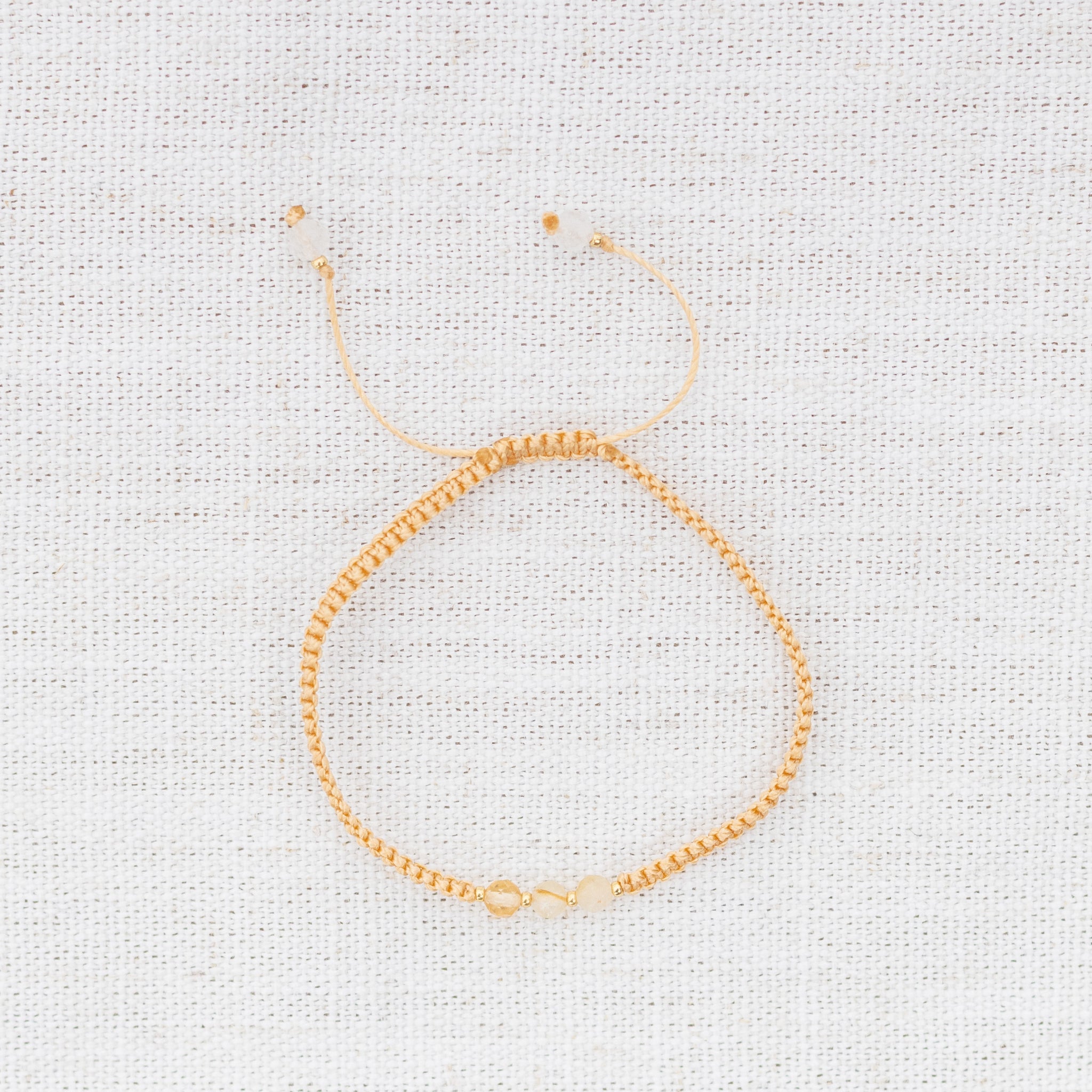 Intuitive Charms Eos's Guard Citrine Braided natural Crystal beaded custom Bracelet in gold and yellow cord on a light fabric background