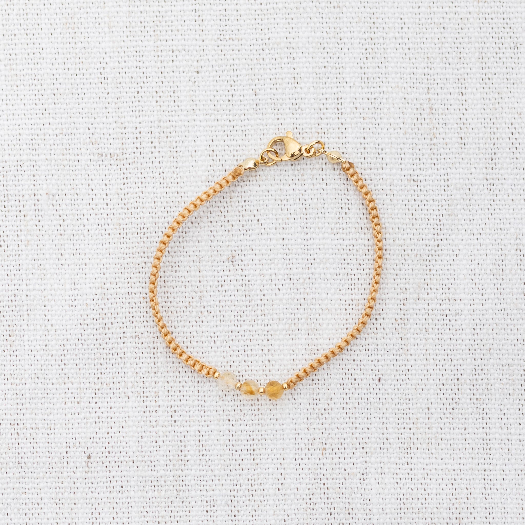 Intuitive Charms Eos's Guard Citrine Braided natural Crystal beaded custom Bracelet in gold and yellow cord and clasp on a light fabric background