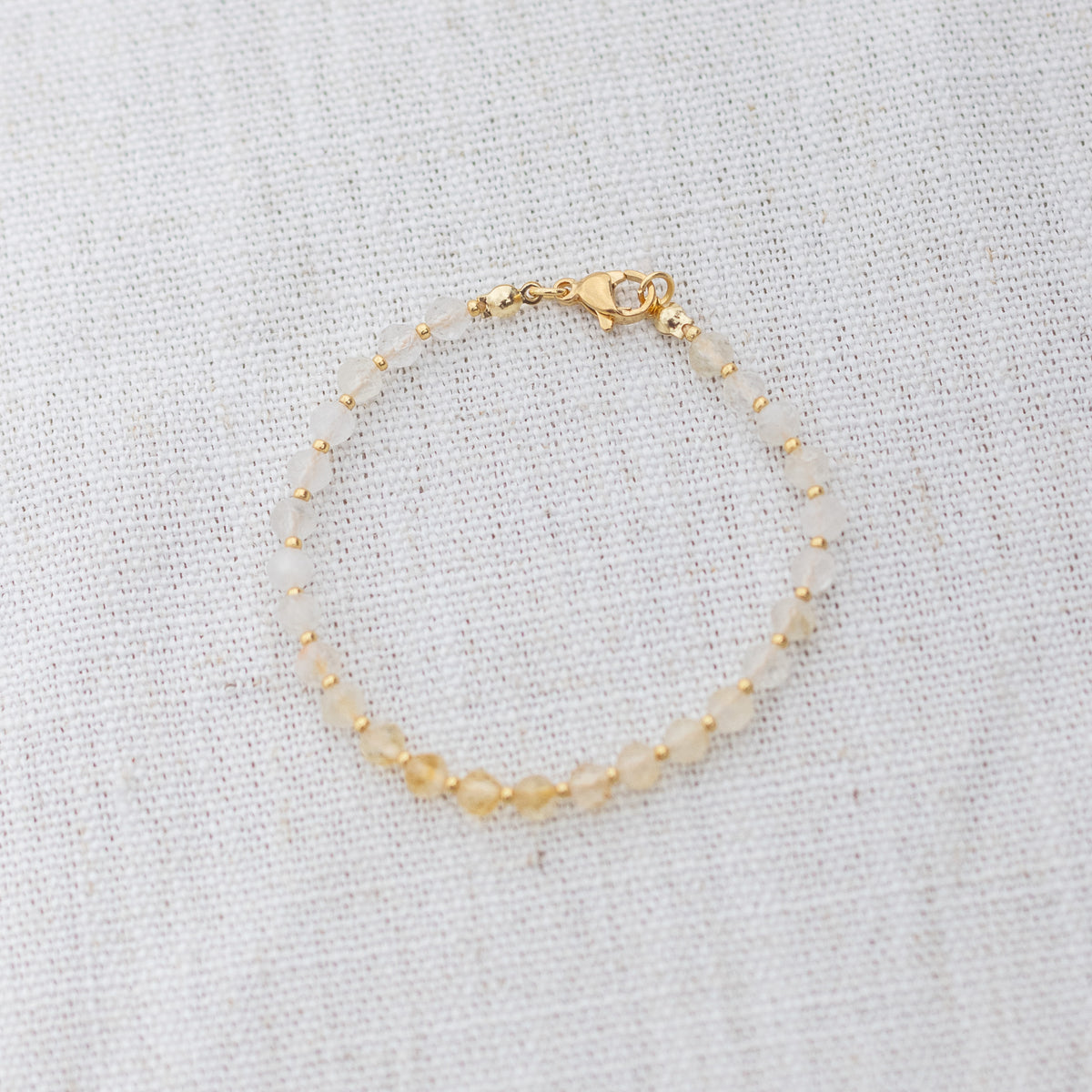 Intuitive Charms Eos's Glow Citrine Braided natural Crystal beaded custom Bracelet in gold and yellow cord and clasp on a light fabric background