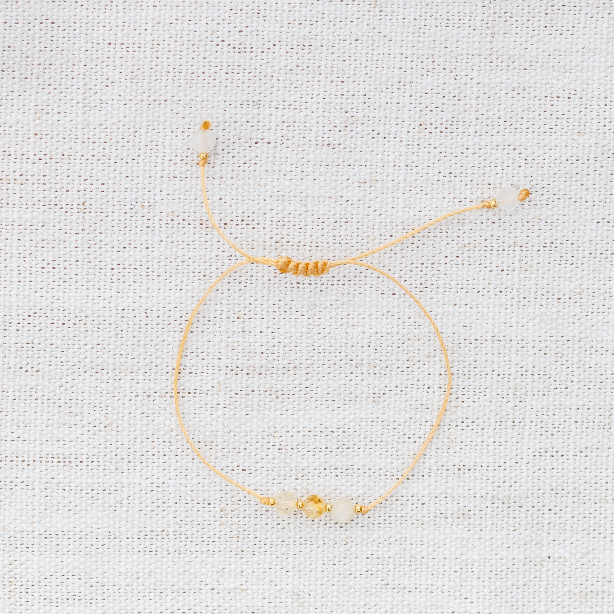 Intuitive Charms Eos's Mist Citrine Braided natural Crystal beaded custom Bracelet in gold and yellow cord on a light fabric background