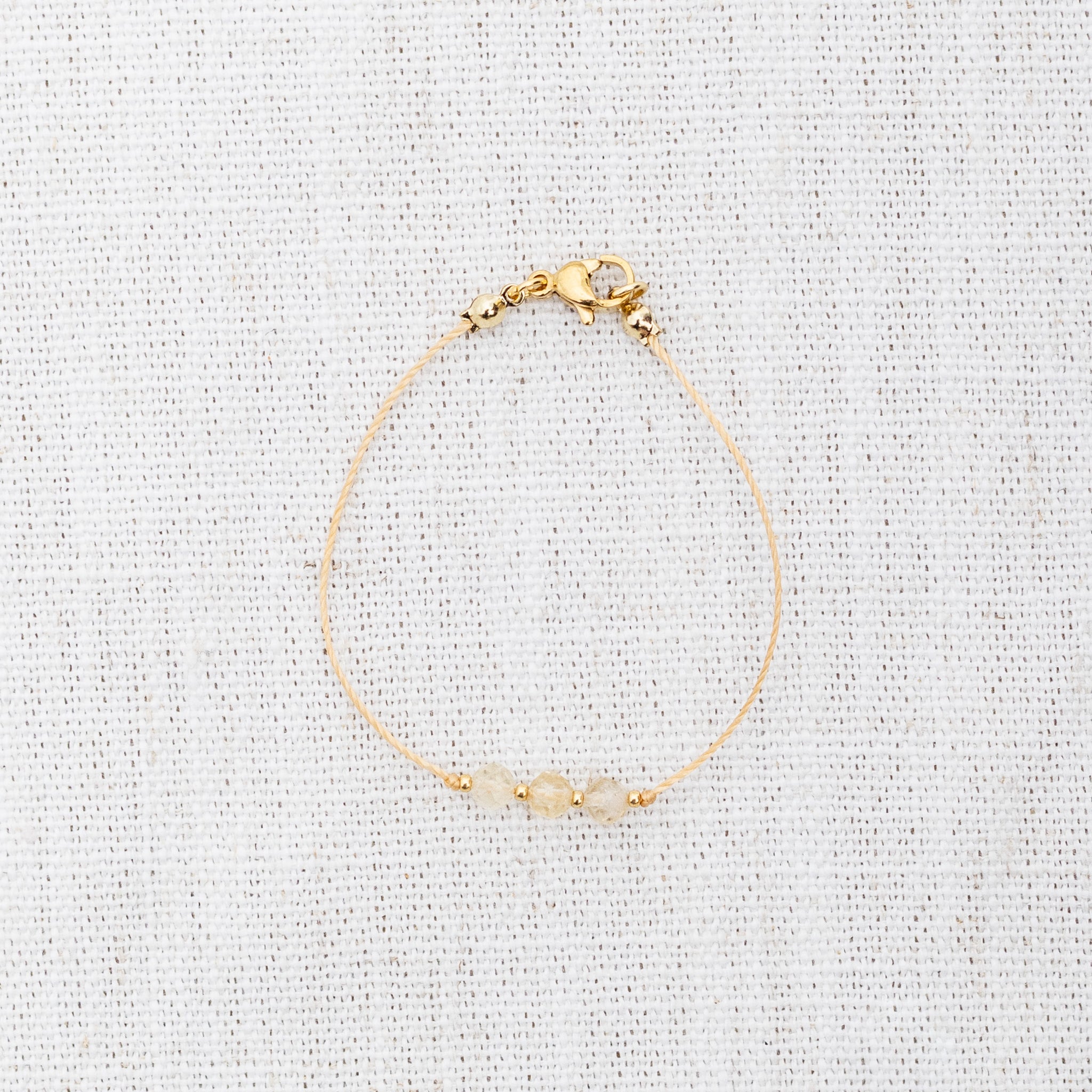 Intuitive Charms Eos's Mist Citrine Braided natural Crystal beaded custom Bracelet in gold and yellow cord and clasp on a light fabric background