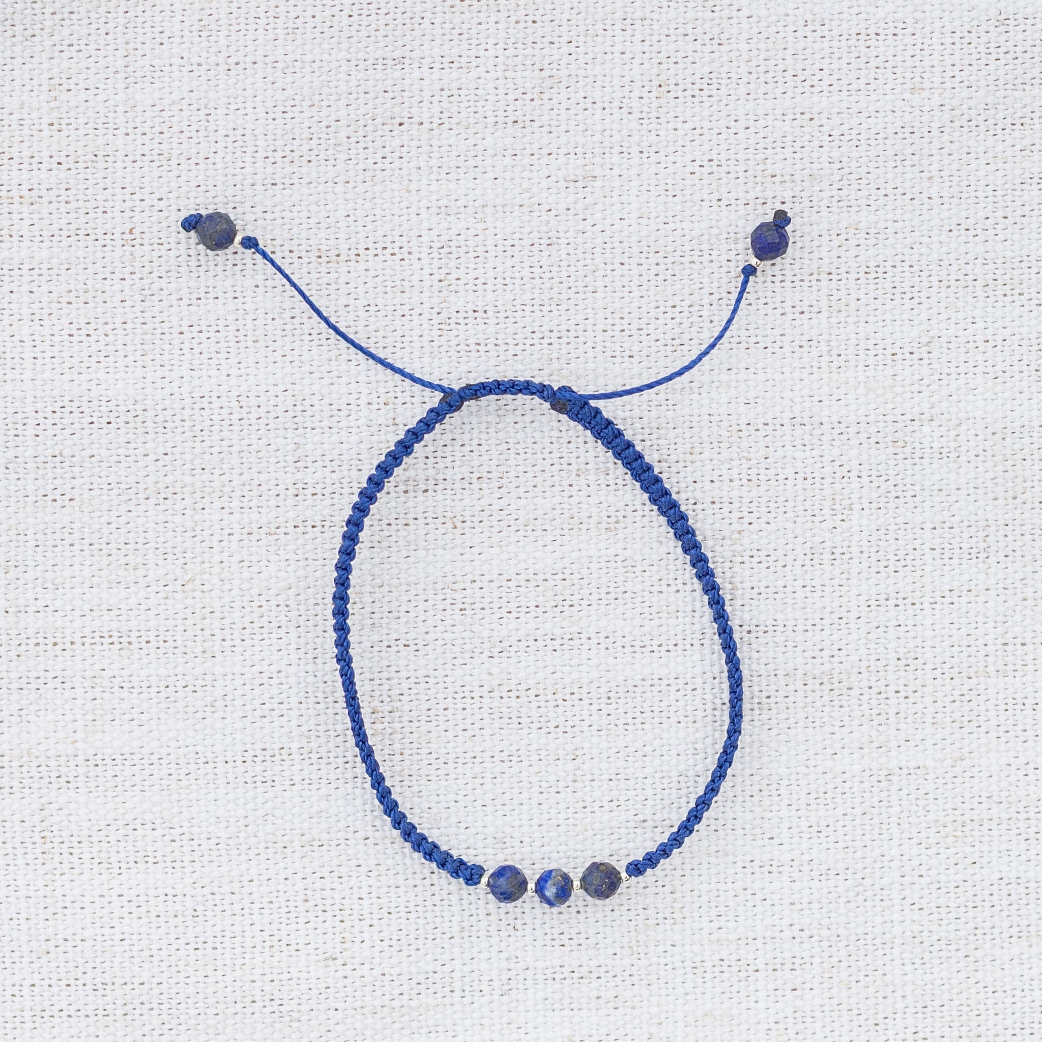 Intuitive Charms Amphitrite's Guard Lapis Lazuli Braided natural Crystal beaded custom Bracelet in silver and deep blue cord on a light fabric background