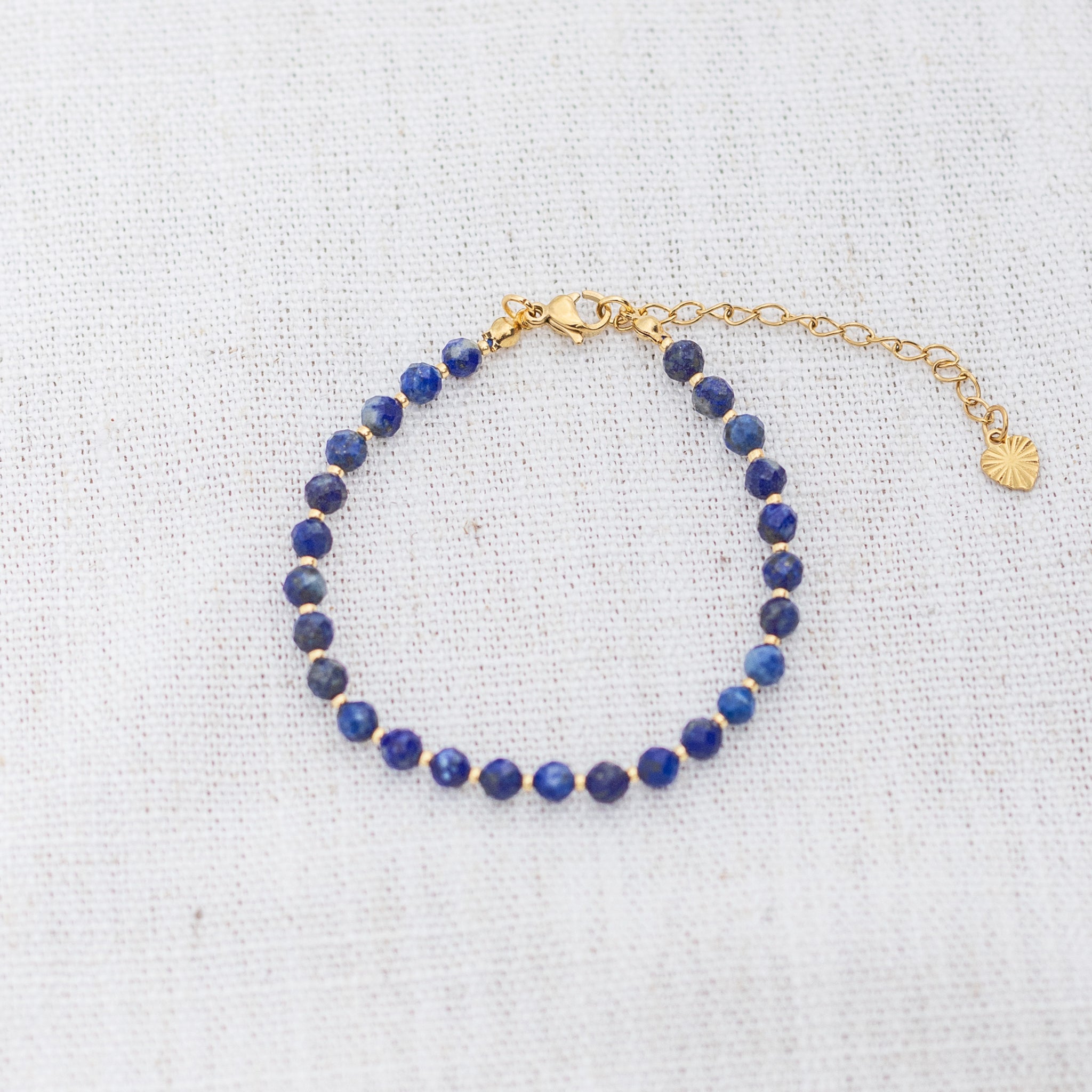 Intuitive Charms Amphitrite's Glow Lapis Lazuli Braided natural Crystal beaded custom Bracelet in gold and deep blue cord and clasp extension on a light fabric background