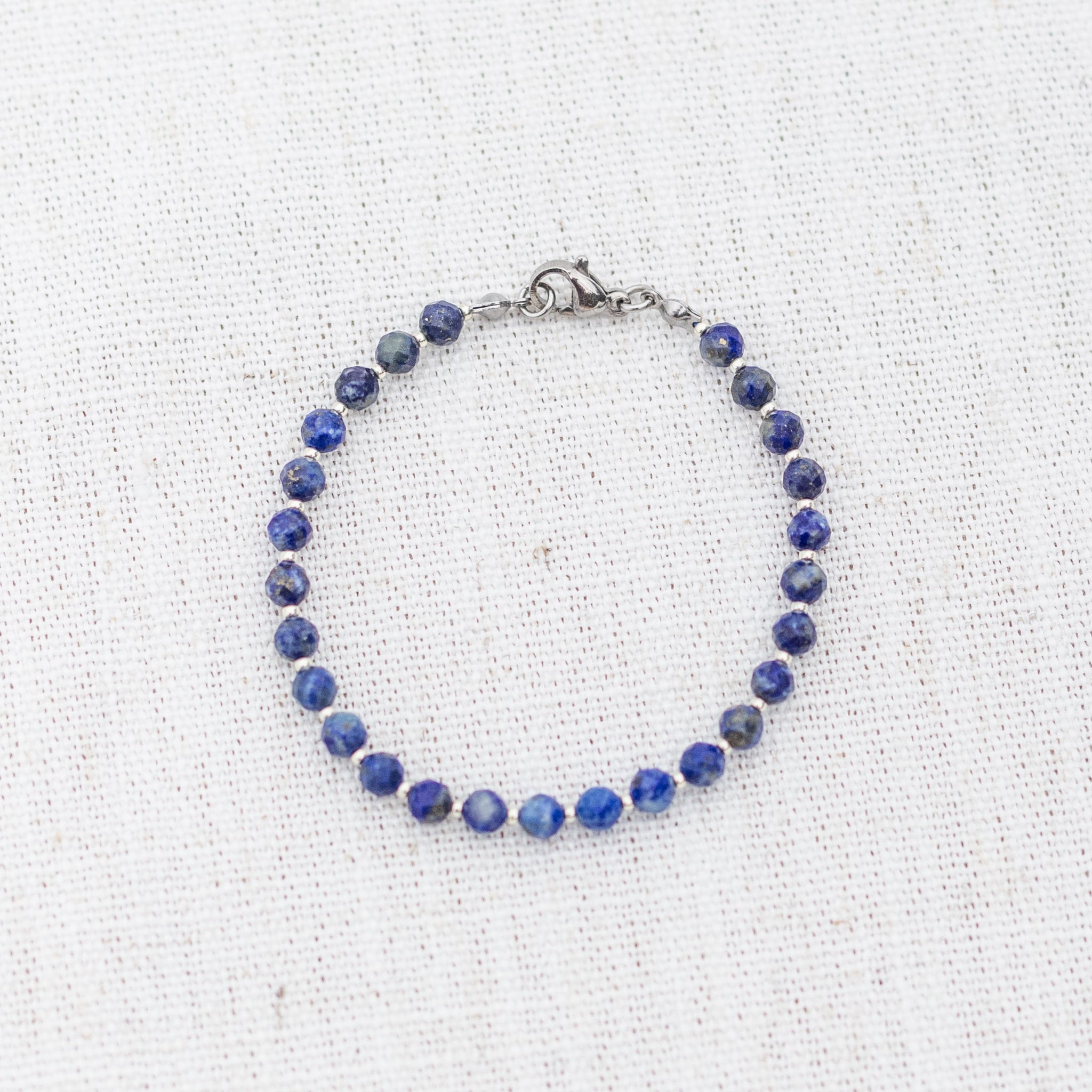 Intuitive Charms Amphitrite's Glow Lapis Lazuli Braided natural Crystal beaded custom Bracelet in silver and deep blue cord and clasp on a light fabric background