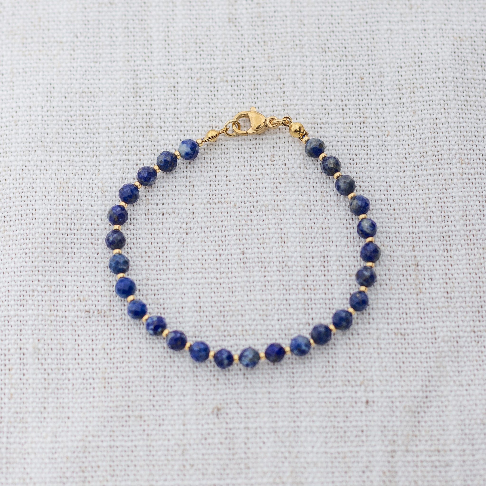 Intuitive Charms Amphitrite's Glow Lapis Lazuli Braided natural Crystal beaded custom Bracelet in gold and deep blue cord and clasp on a light fabric background