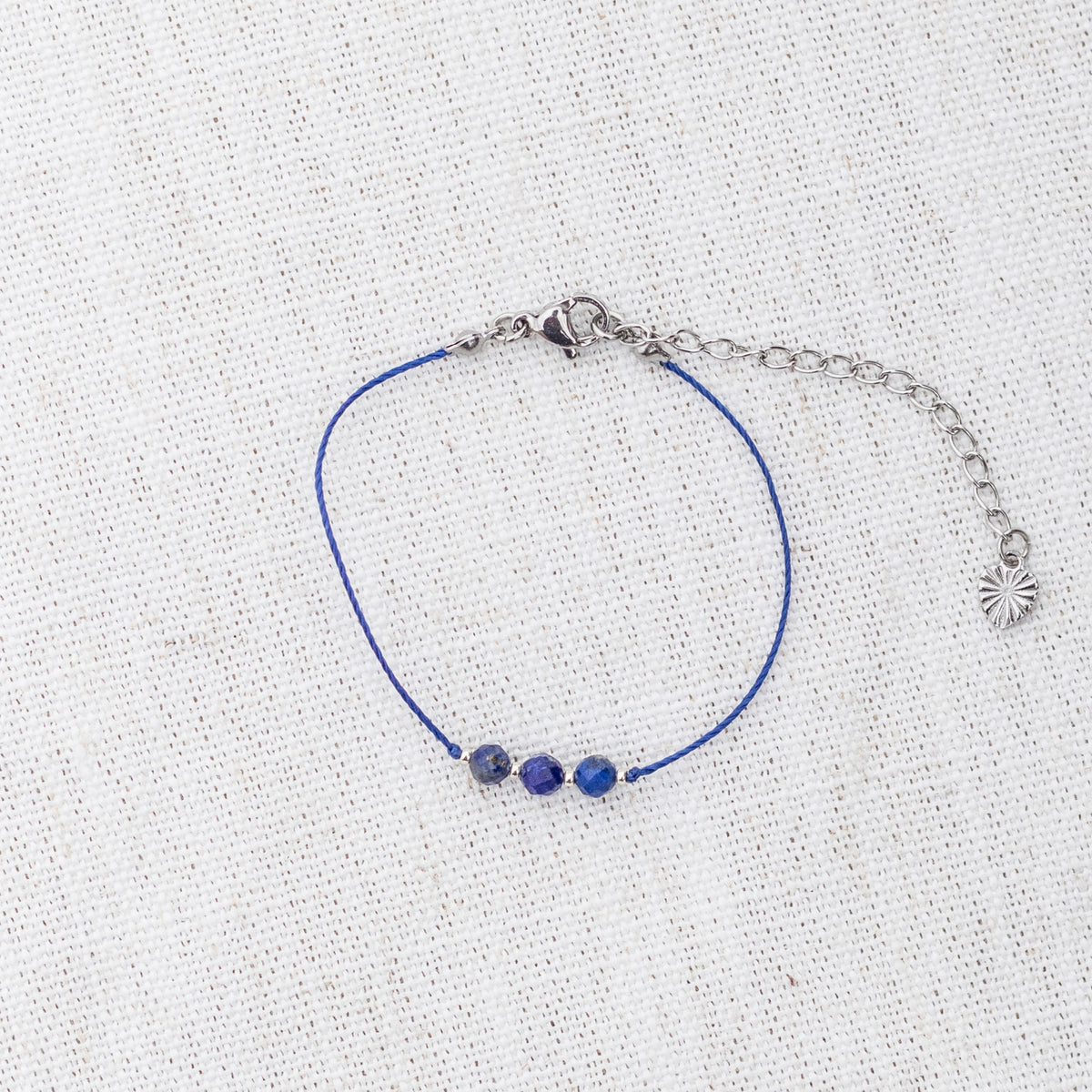 Intuitive Charms Amphitrite's Mist Lapis Lazuli Braided natural Crystal beaded custom Bracelet in silver and deep blue cord and clasp extension on a light fabric background