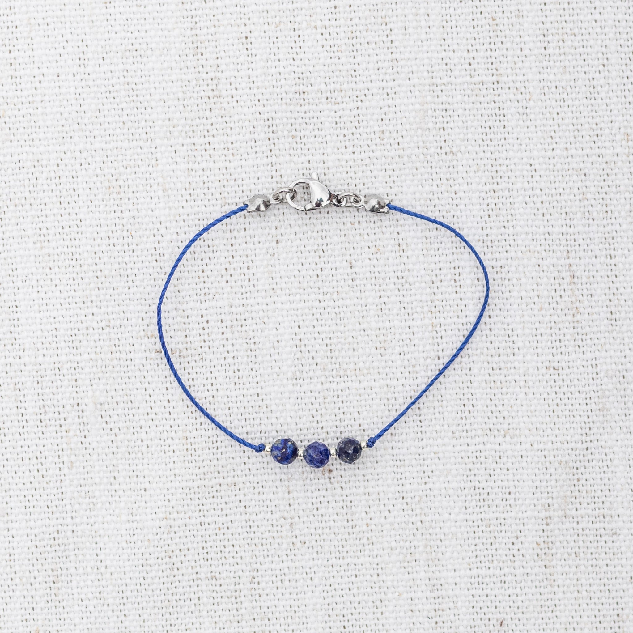 Intuitive Charms Amphitrite's Mist Lapis Lazuli Braided natural Crystal beaded custom Bracelet in silver and deep blue cord and clasp on a light fabric background