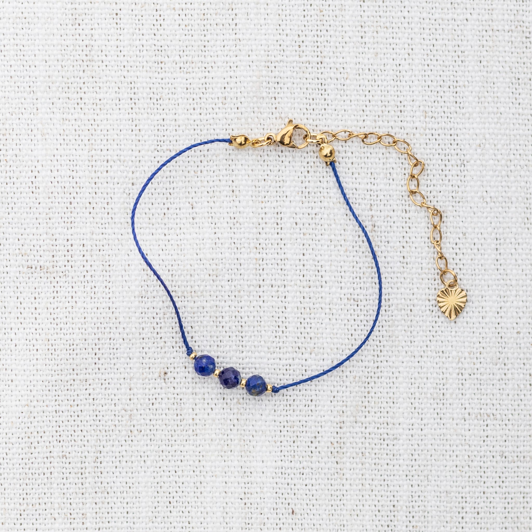 Intuitive Charms Amphitrite's Mist Lapis Lazuli Braided natural Crystal beaded custom Bracelet in gold and deep blue cord and clasp extension on a light fabric background