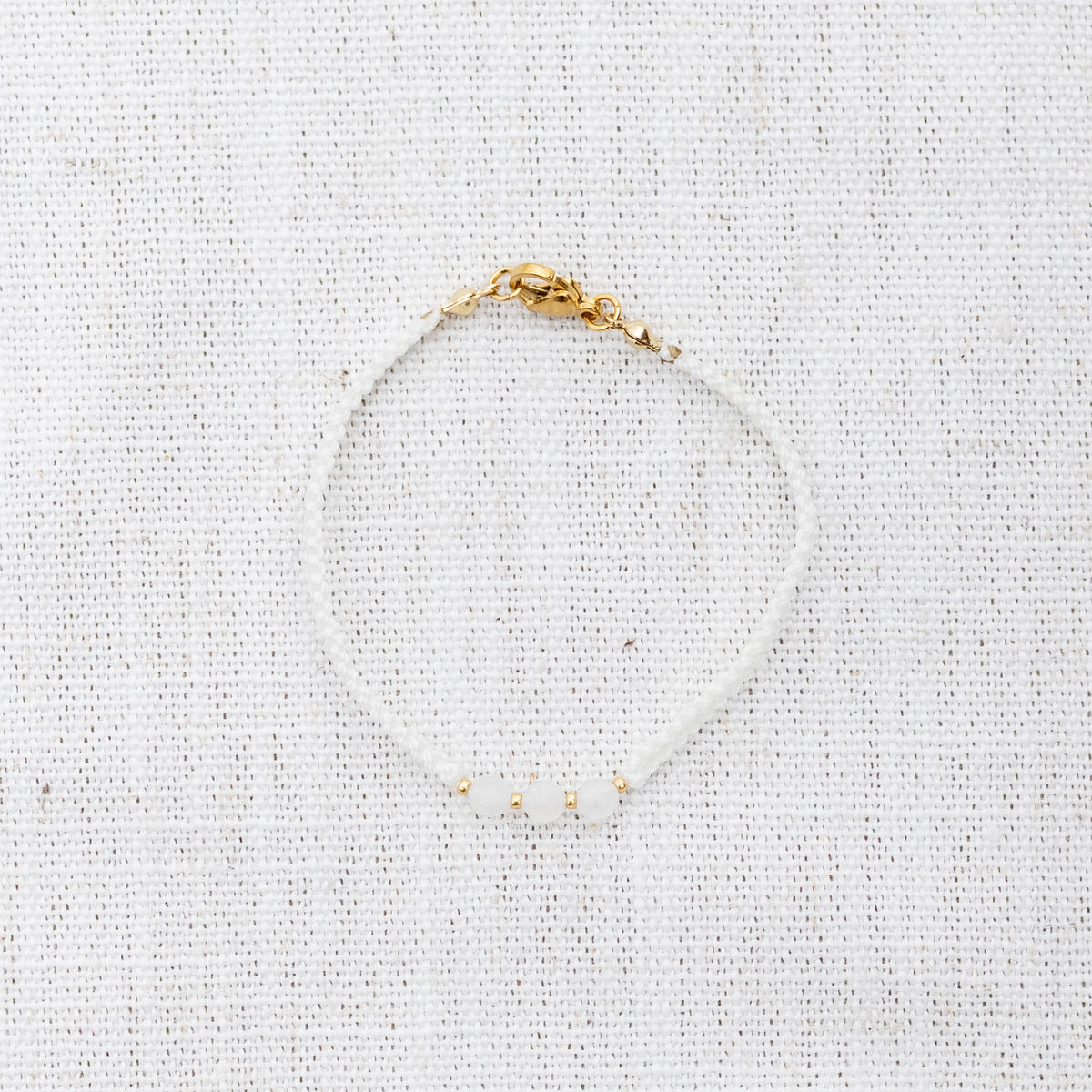 Intuitive Charms Selene's Guard Moonstone Braided natural Crystal beaded custom Bracelet in gold and white cord and clasp on a light fabric background