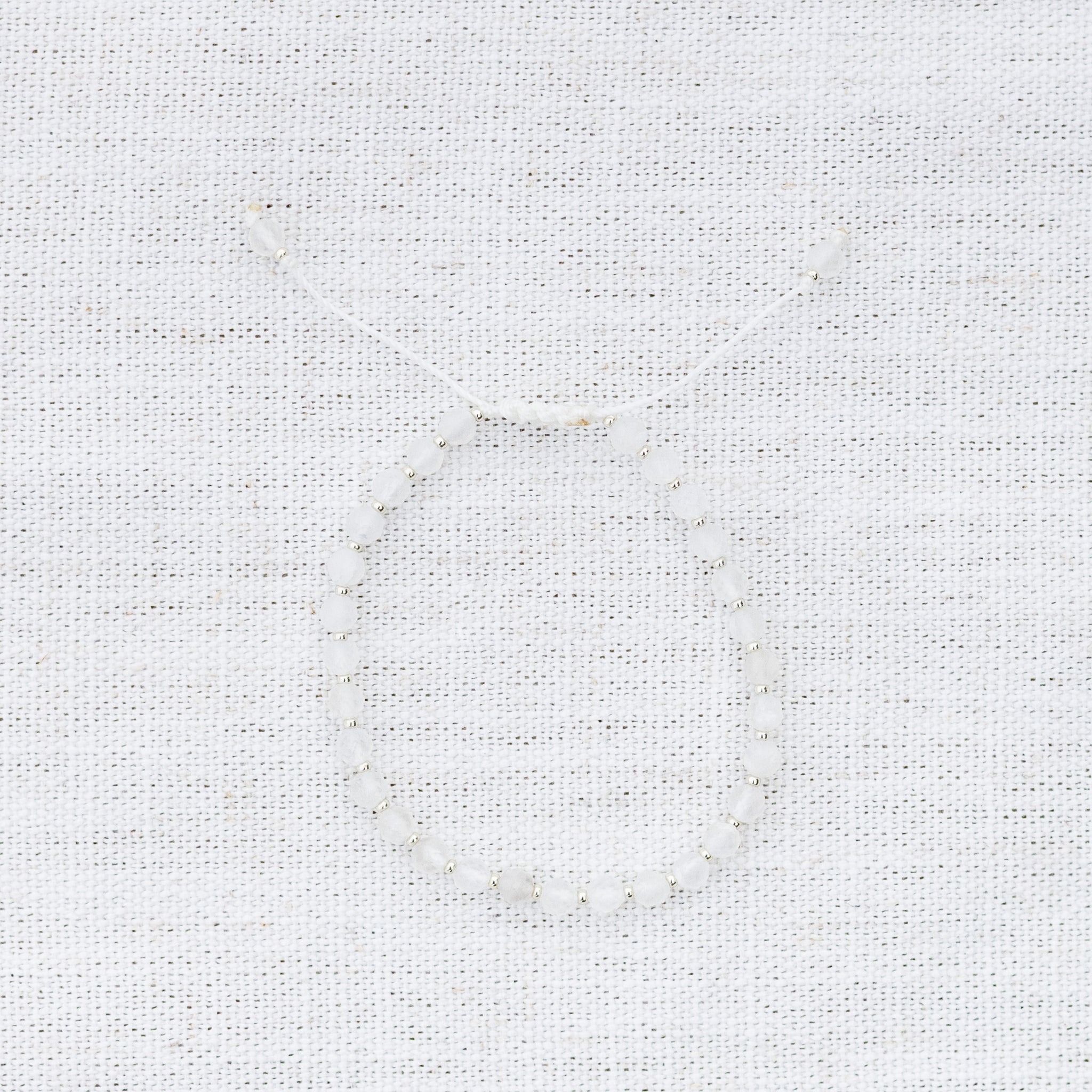Intuitive Charms Selene's Glow Moonstone Braided natural Crystal beaded custom Bracelet in silver and white cord on a light fabric background