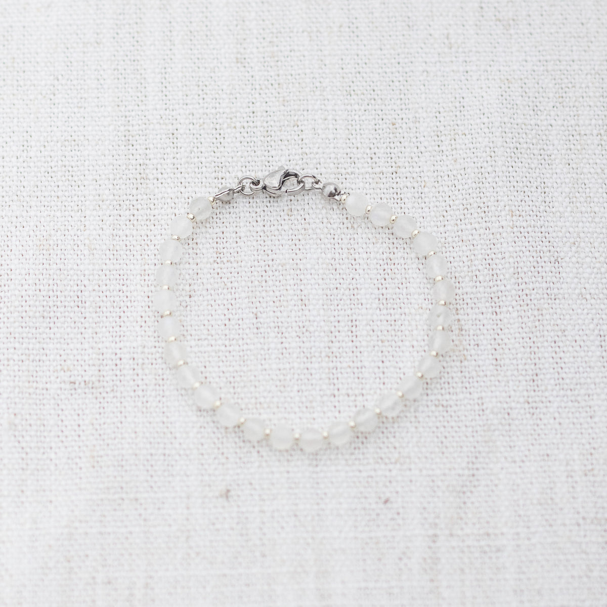 Intuitive Charms Selene's Glow Moonstone Braided natural Crystal beaded custom Bracelet in silver and white cord and clasp on a light fabric background