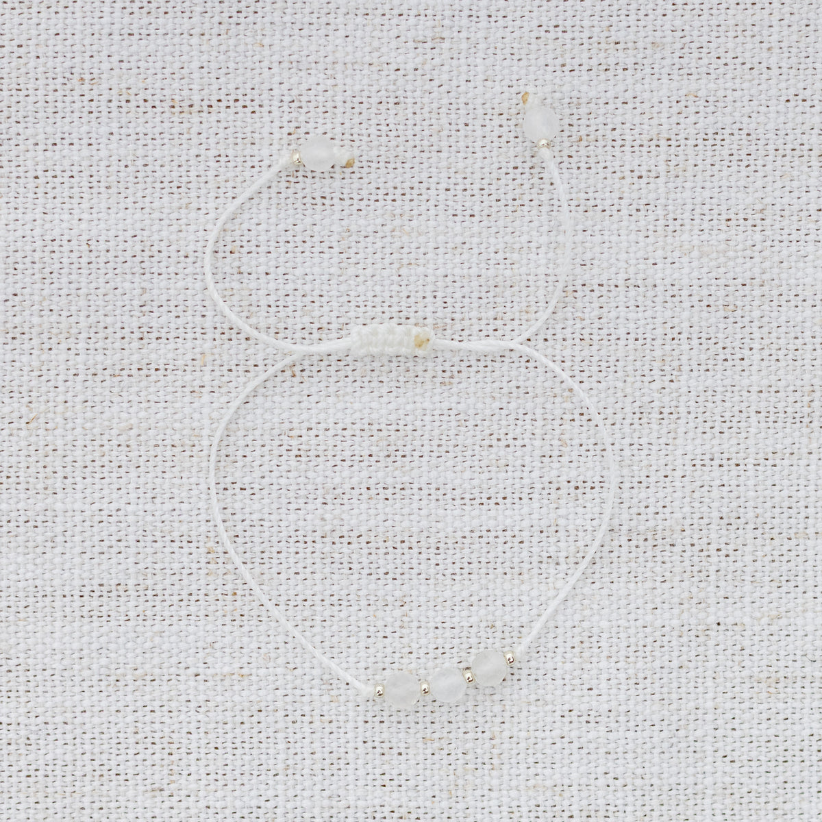 Intuitive Charms Selene's Mist Moonstone Braided natural Crystal beaded custom Bracelet in silver and white cord on a light fabric background