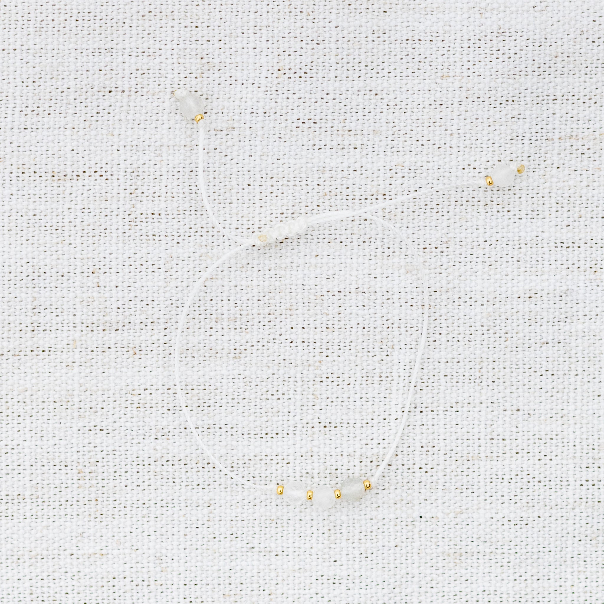 Intuitive Charms Selene's Mist Moonstone Braided natural Crystal beaded custom Bracelet in gold and white cord on a light fabric background