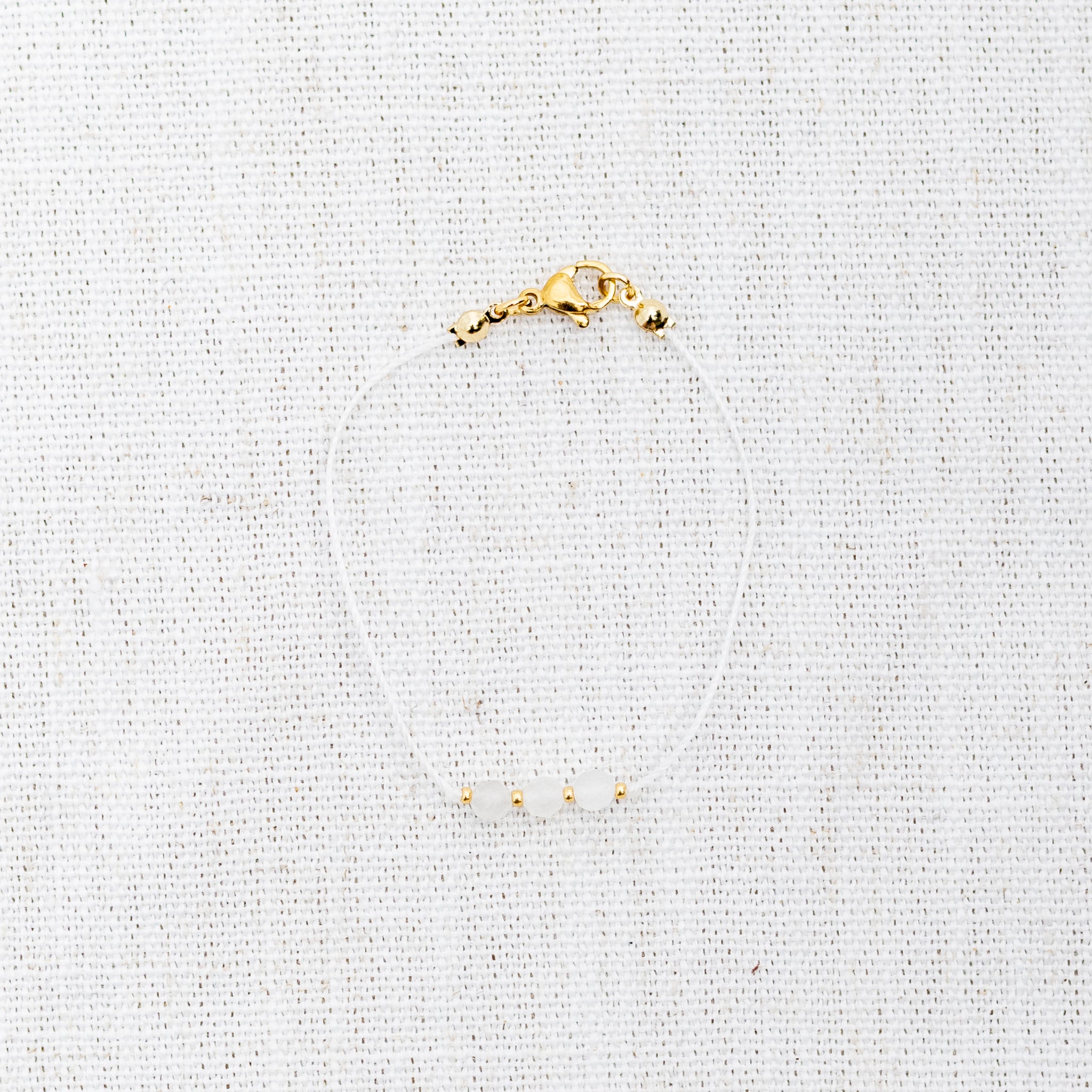 Intuitive Charms Selene's Mist Moonstone Braided natural Crystal beaded custom Bracelet in gold and white cord and clasp on a light fabric background