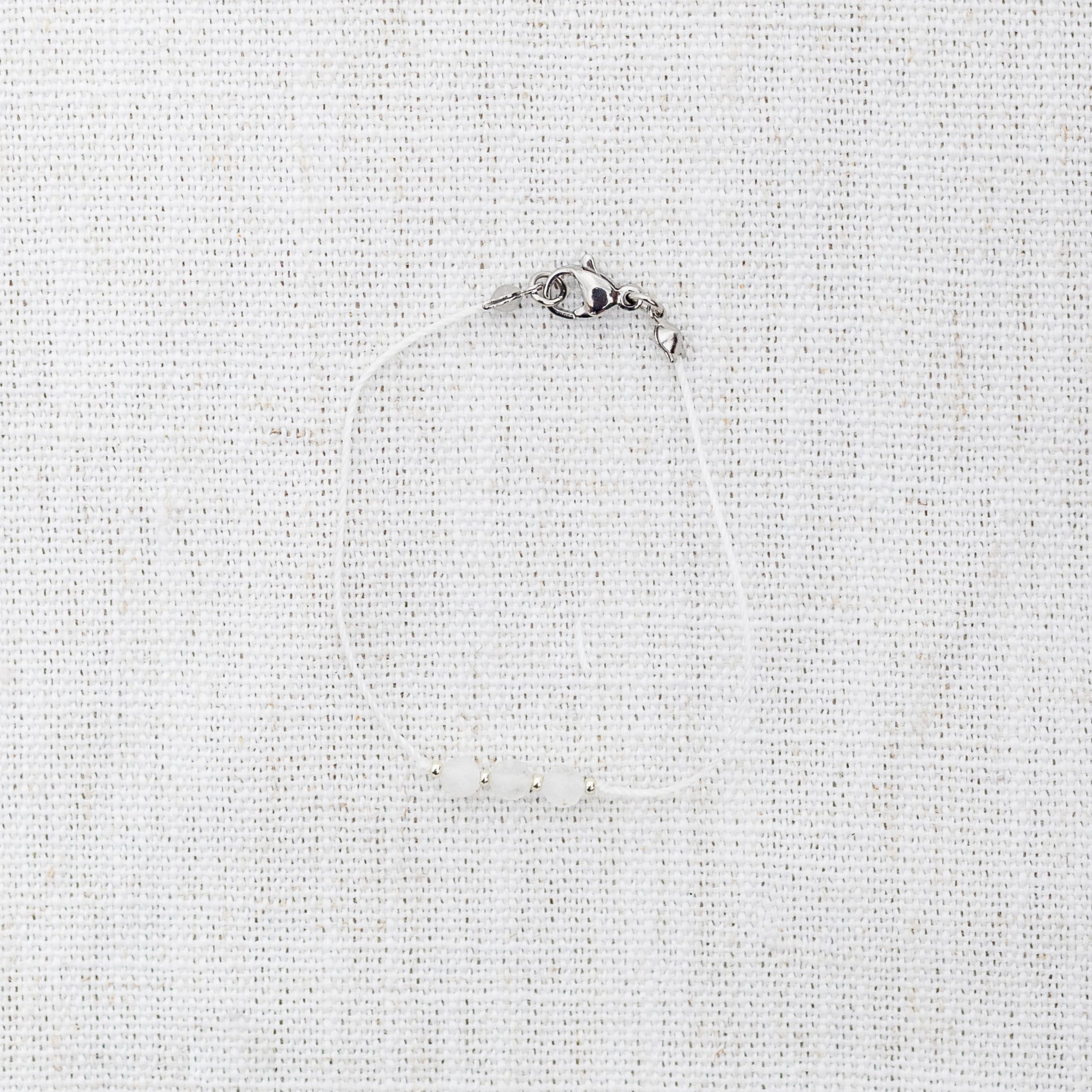 Intuitive Charms Selene's Mist Moonstone Braided natural Crystal beaded custom Bracelet in silver and white cord and clasp on a light fabric background