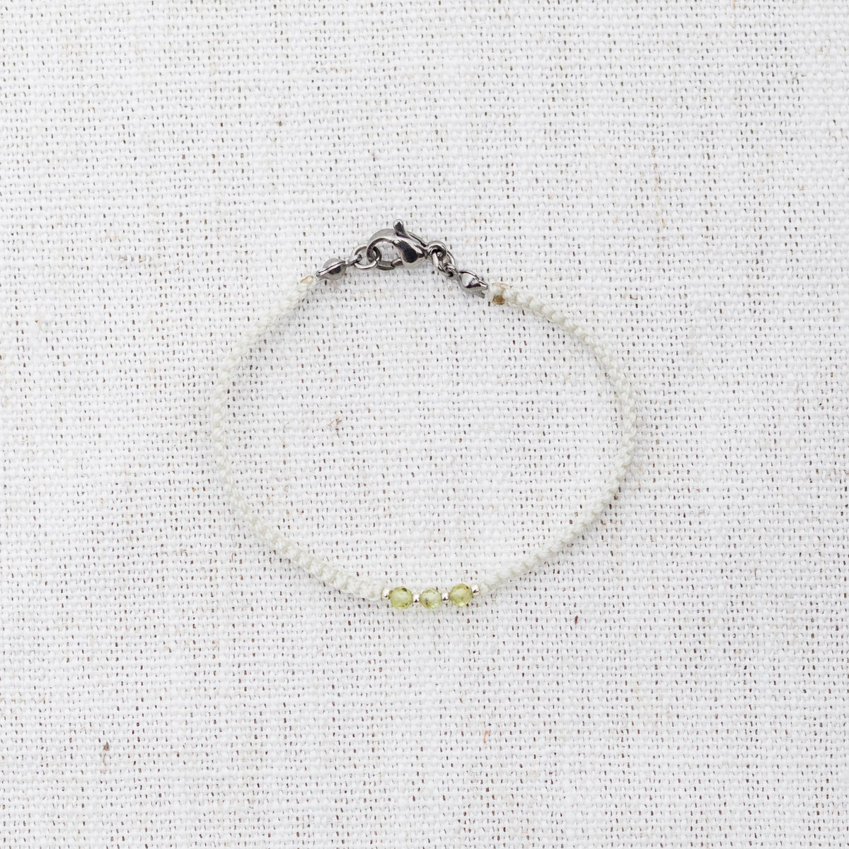 Intuitive Charms Nerina's Guard Peridot Braided natural Crystal beaded custom Bracelet in silver and light mint cord and clasp on a light fabric background