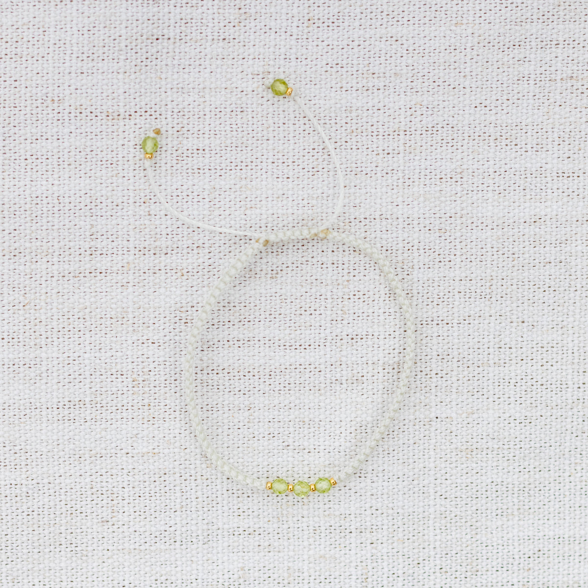 Intuitive Charms Nerina's Guard Peridot Braided natural Crystal beaded custom Bracelet in gold and light mint cord on a light fabric background