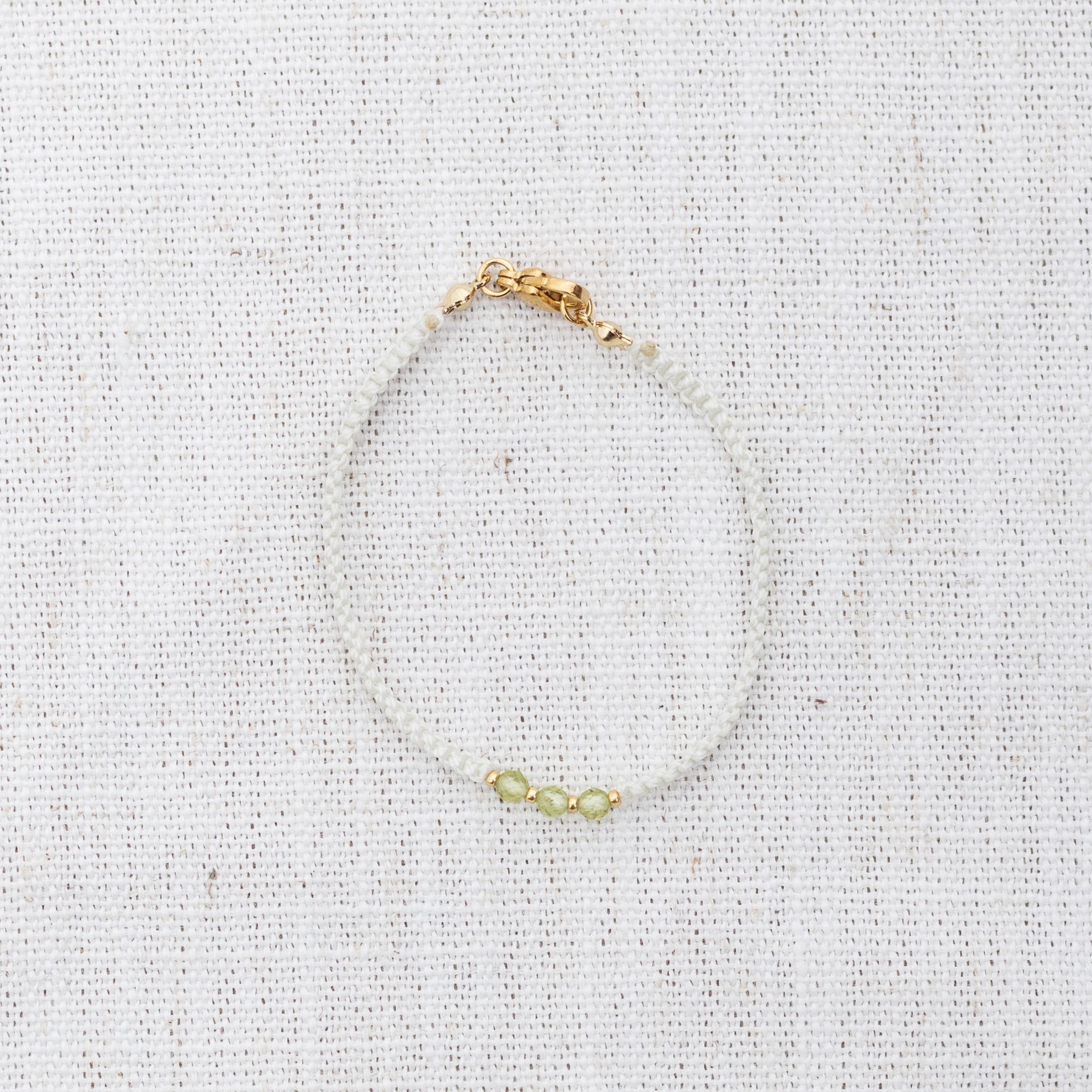 Intuitive Charms Nerina's Guard Peridot Braided natural Crystal beaded custom Bracelet in gold and light mint cord and clasp on a light fabric background