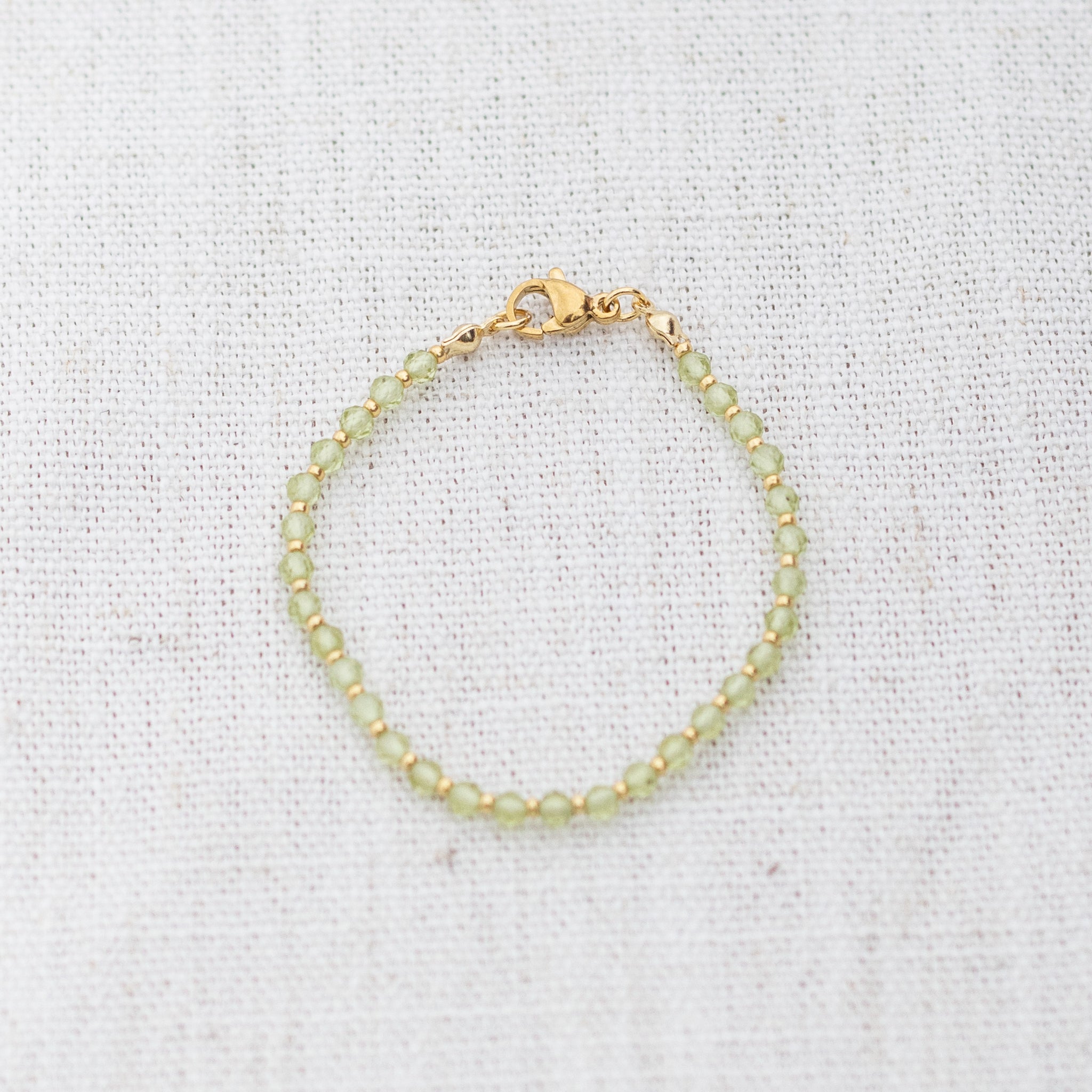 Intuitive Charms Nerina's Glow Peridot Braided natural Crystal beaded custom Bracelet in gold and light mint cord and clasp on a light fabric background