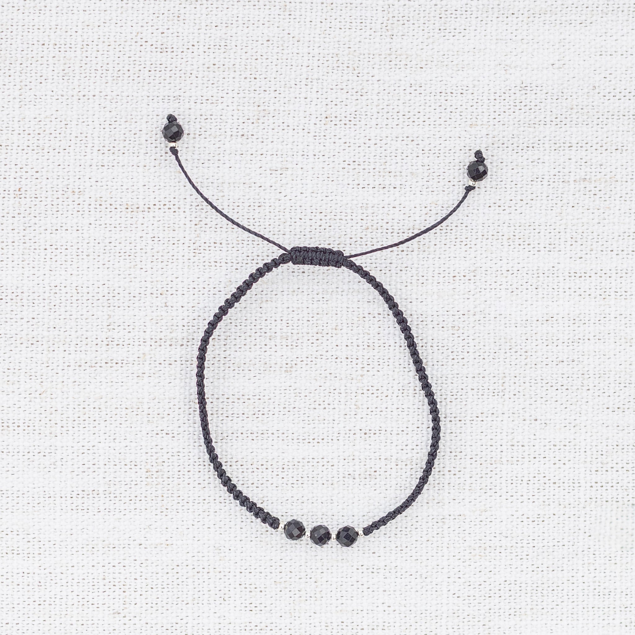 Intuitive Charms Ceto's Guard Black tourmaline Braided natural Crystal beaded custom Bracelet in silver and black cord on a light fabric background