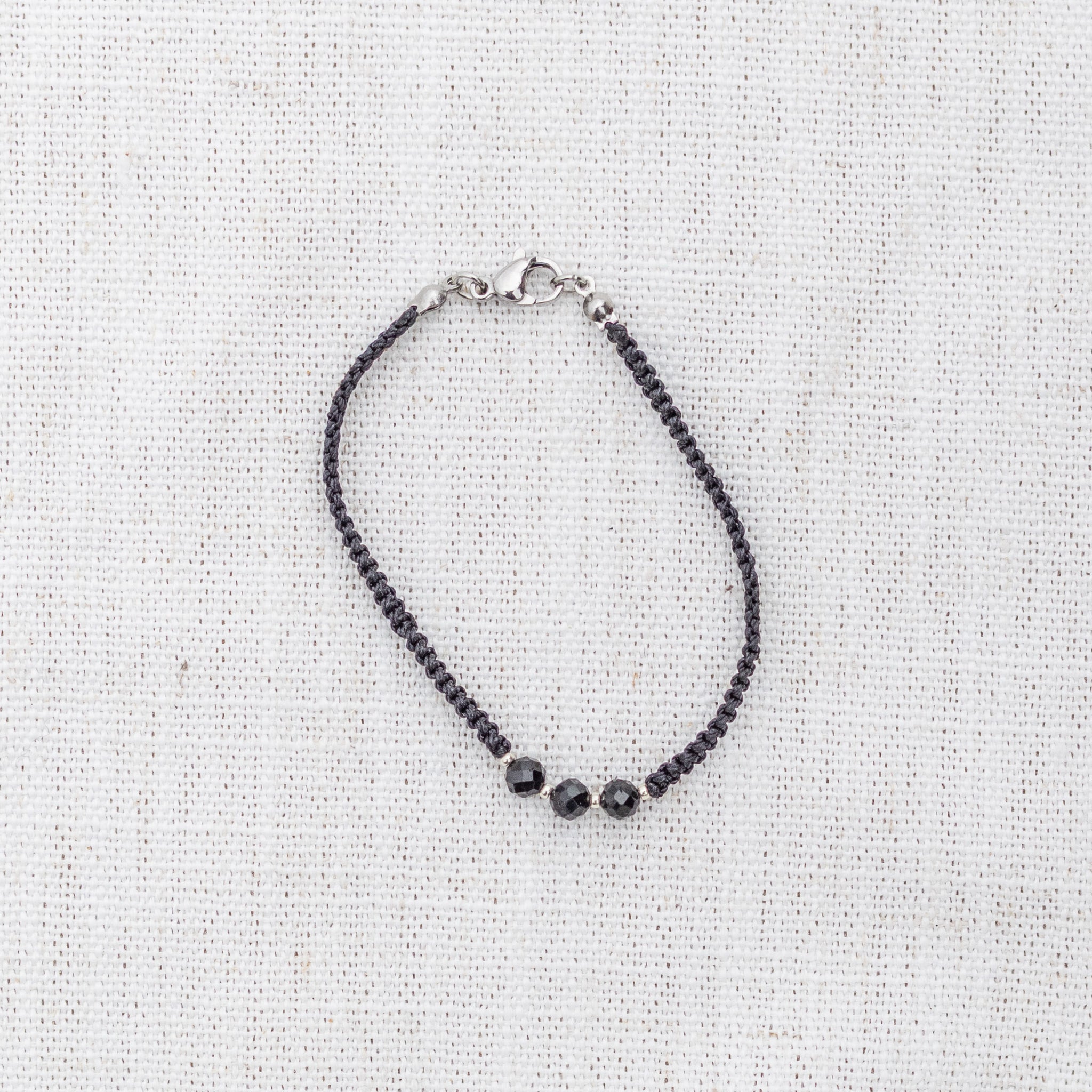 Intuitive Charms Ceto's Guard Black tourmaline Braided natural Crystal beaded custom Bracelet in silver and black cord and clasp on a light fabric background
