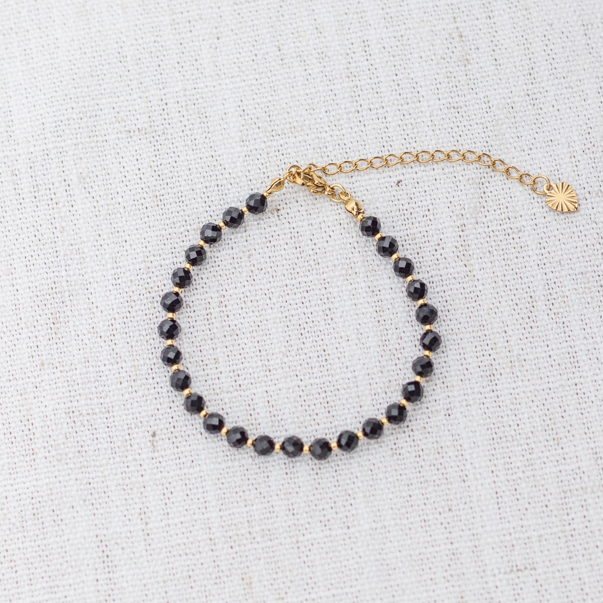 Intuitive Charms Ceto's Glow Apatite Braided natural Crystal beaded custom Bracelet in gold and black cord and clasp extension on a light fabric background