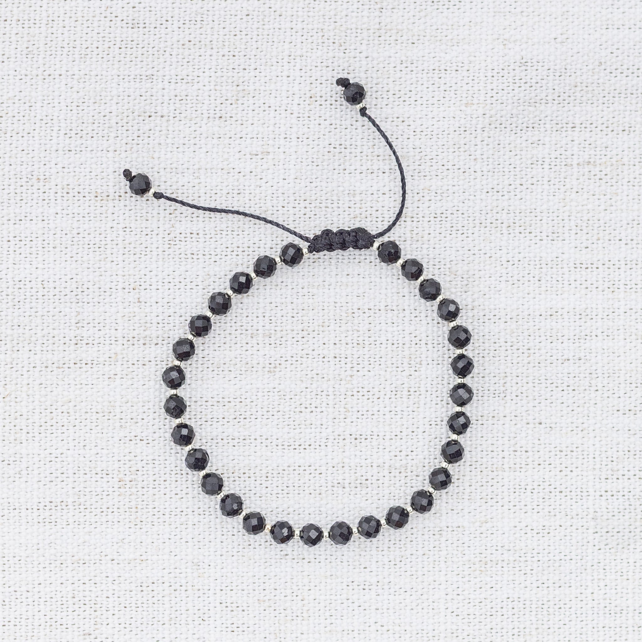 Intuitive Charms Ceto's Glow Apatite Braided natural Crystal beaded custom Bracelet in silver and black cord on a light fabric background