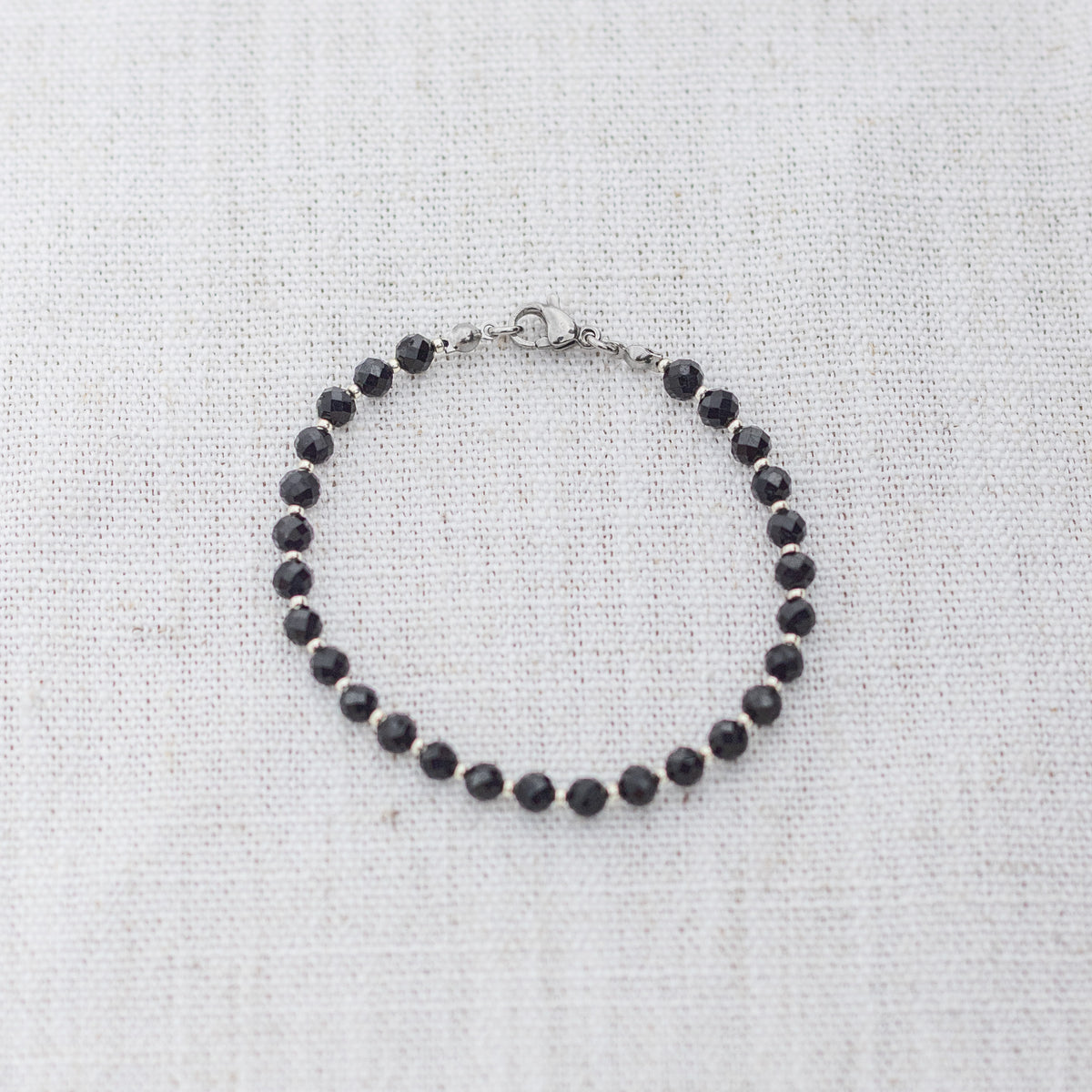 Intuitive Charms Ceto's Glow Apatite Braided natural Crystal beaded custom Bracelet in silver and black cord and clasp on a light fabric background