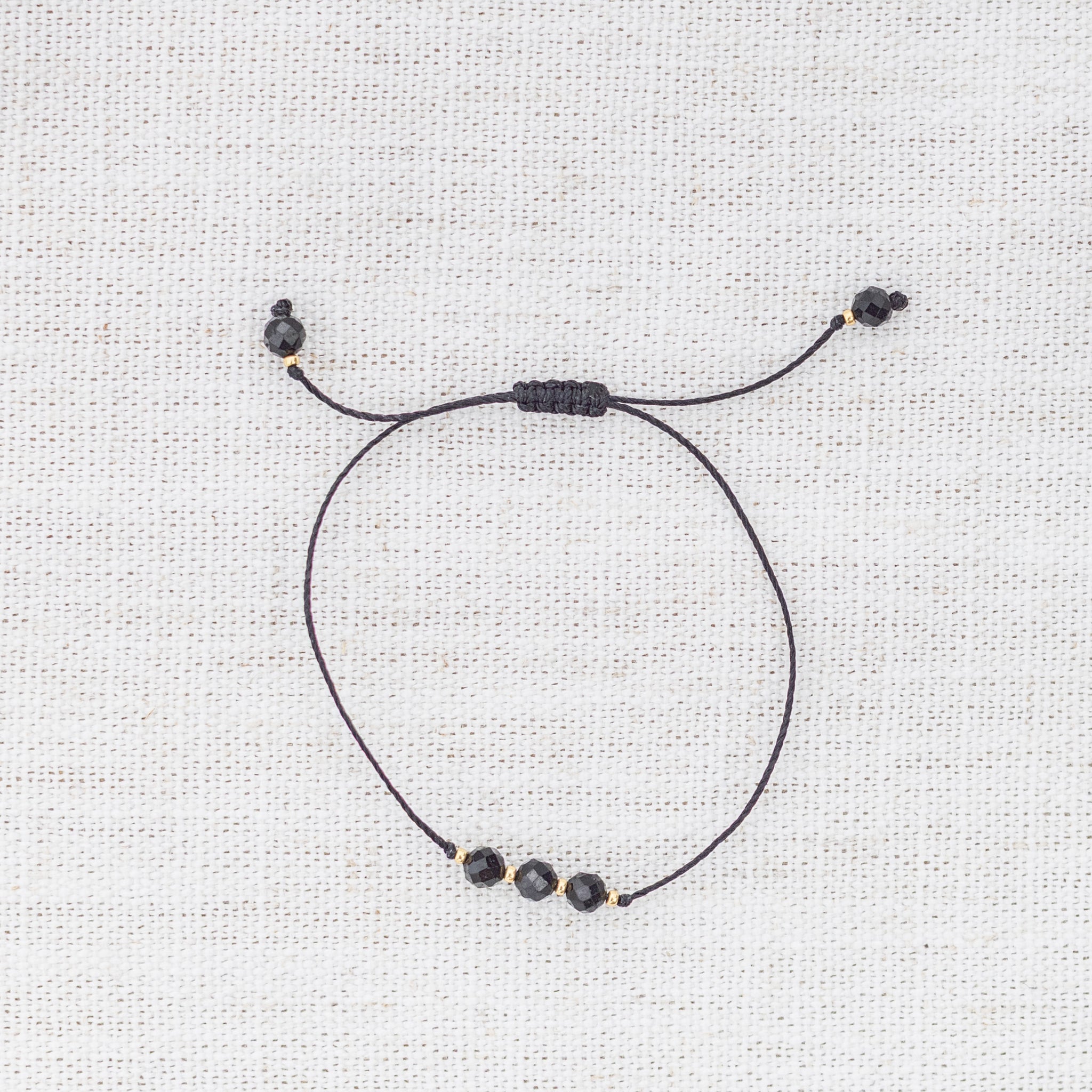 Intuitive Charms Ceto's Mist Black tourmaline Braided natural Crystal beaded custom Bracelet in gold and black cord on a light fabric background