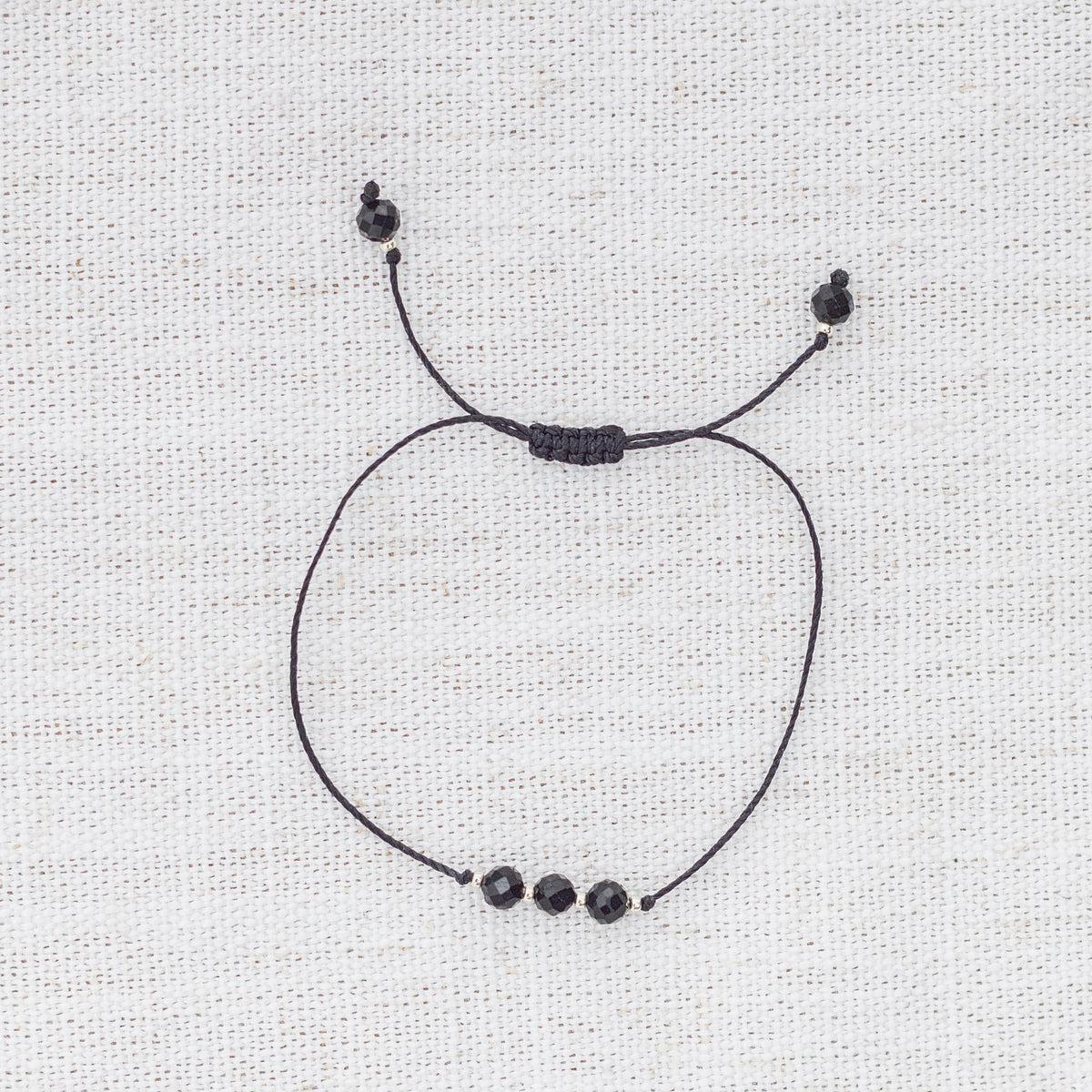 Intuitive Charms Ceto's Mist Black tourmaline Braided natural Crystal beaded custom Bracelet in silver and black cord on a light fabric background