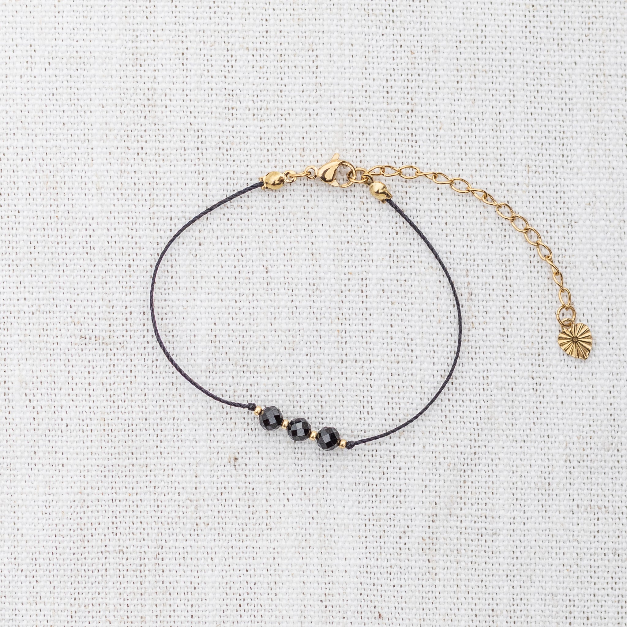 Intuitive Charms Ceto's Mist Black tourmaline Braided natural Crystal beaded custom Bracelet in gold and black cord and clasp extension on a light fabric background
