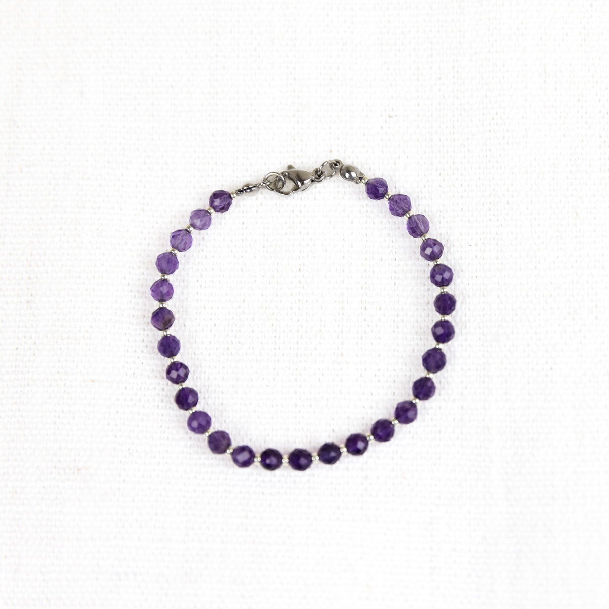 Intuitive Charms Sophia's Glow Amethyst Braided natural Crystal beaded custom Bracelet in silver and purple cord and stainless steel clasp on a light fabric background